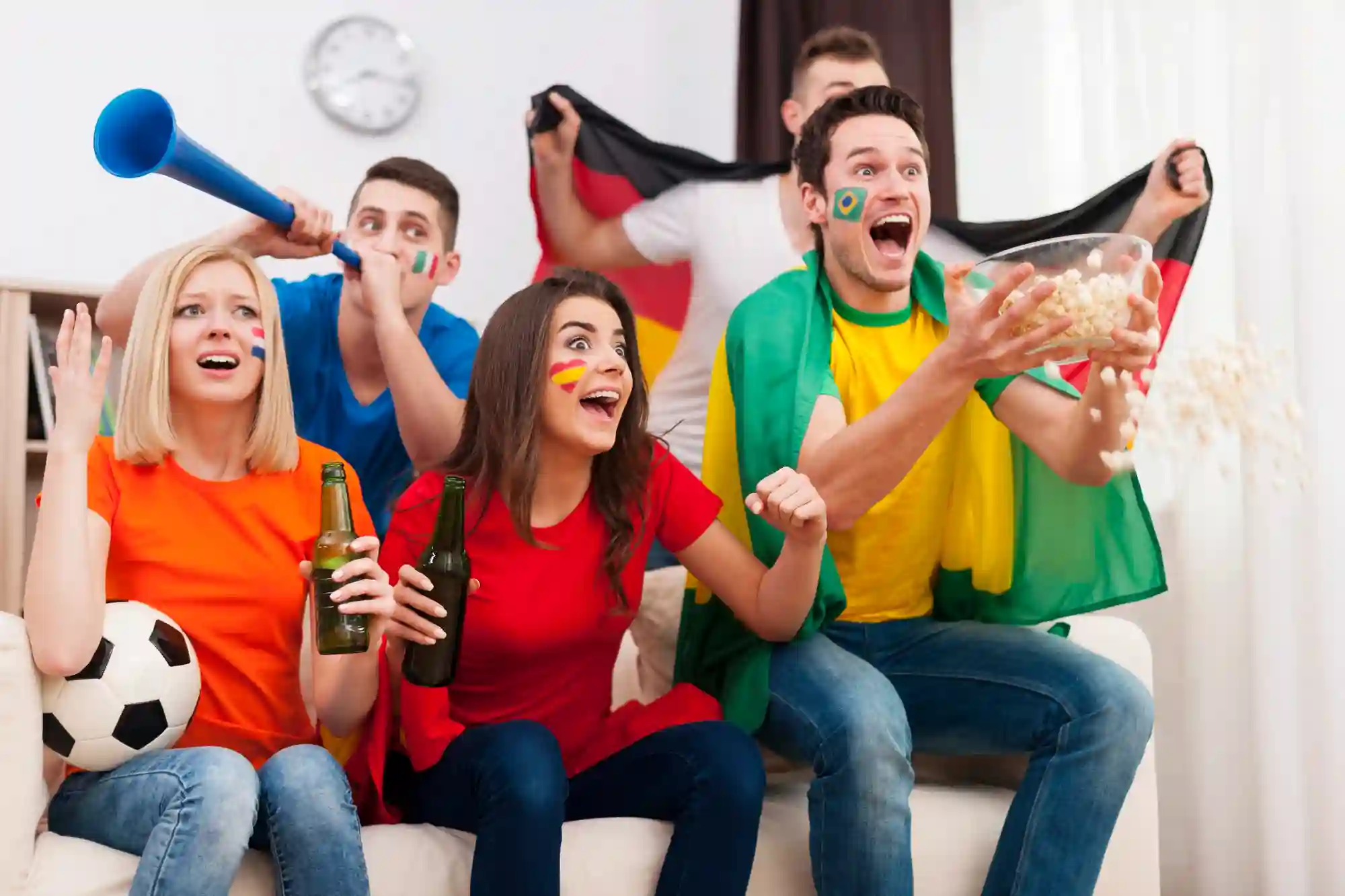 A group of excited multicultural football fans cheer and celebrate while watching a match together at home.