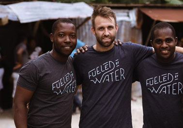 Group of men wearing "Fueled by Water" shirts, smiling outdoors.