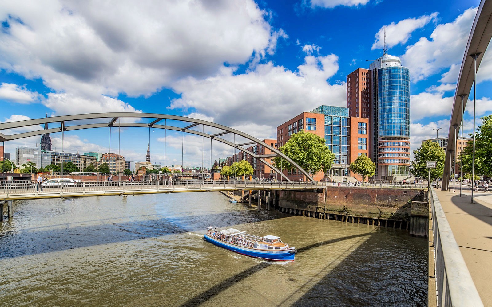 Bådtur under bro på byens havnerundfart med moderne bygninger i baggrunden.