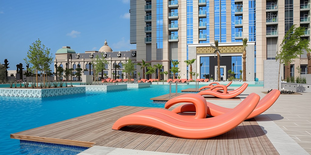 Aerial view of a swimming pool surrounded by palm trees, with Noora Tower visible in the background.