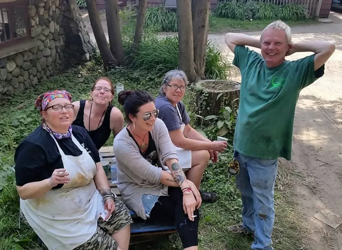 A group of five people relax outdoors among trees, enjoying a casual moment together.