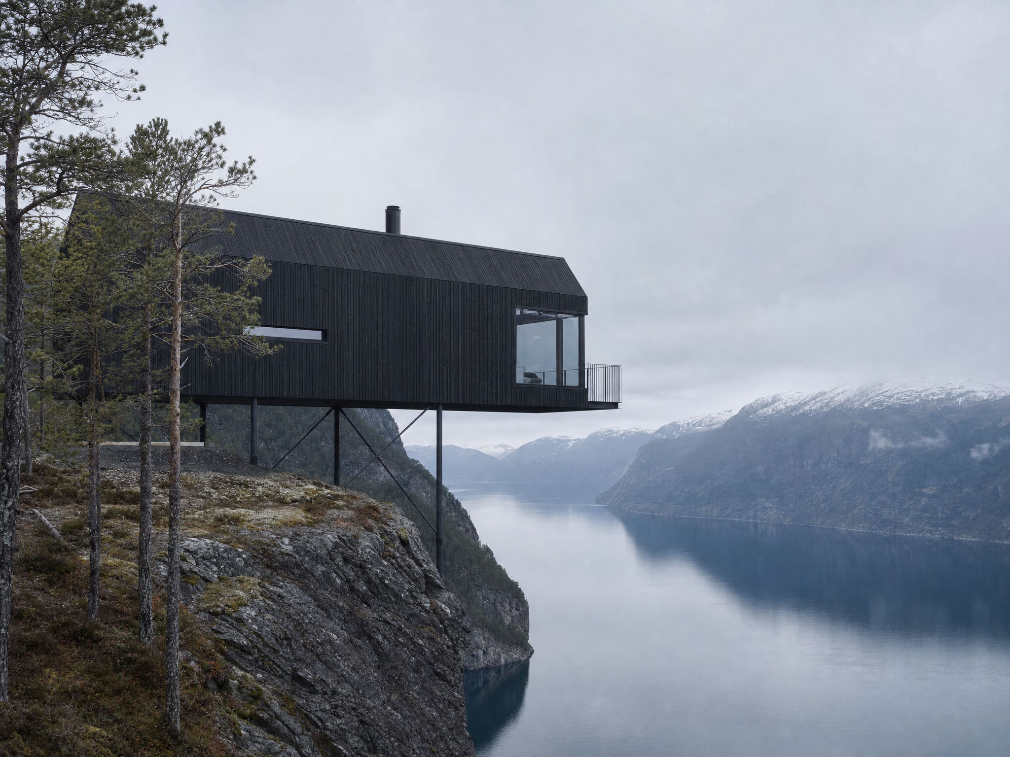 Dark timber cabin on stilts above a still fjord