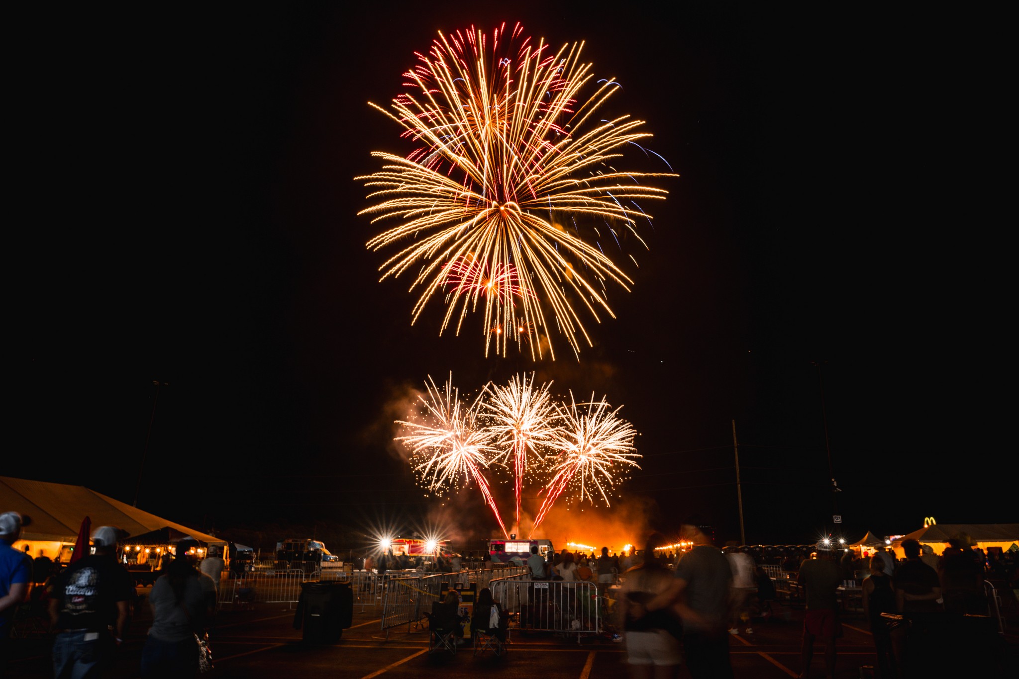 Bright fireworks exploding in the night sky over a festival crowd and tents, capturing a celebratory event.