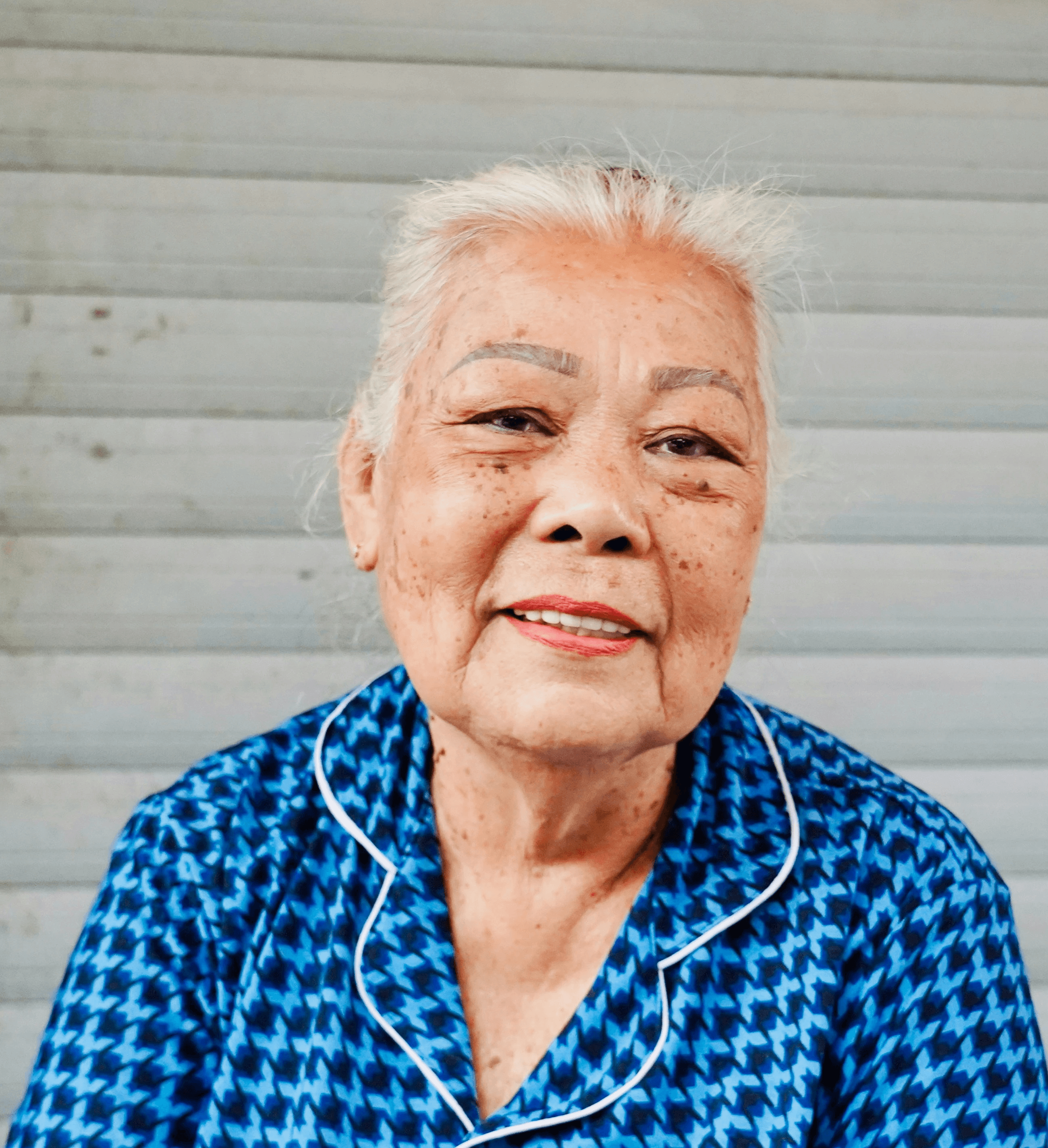 Elderly woman with white hair in blue patterned shirt.