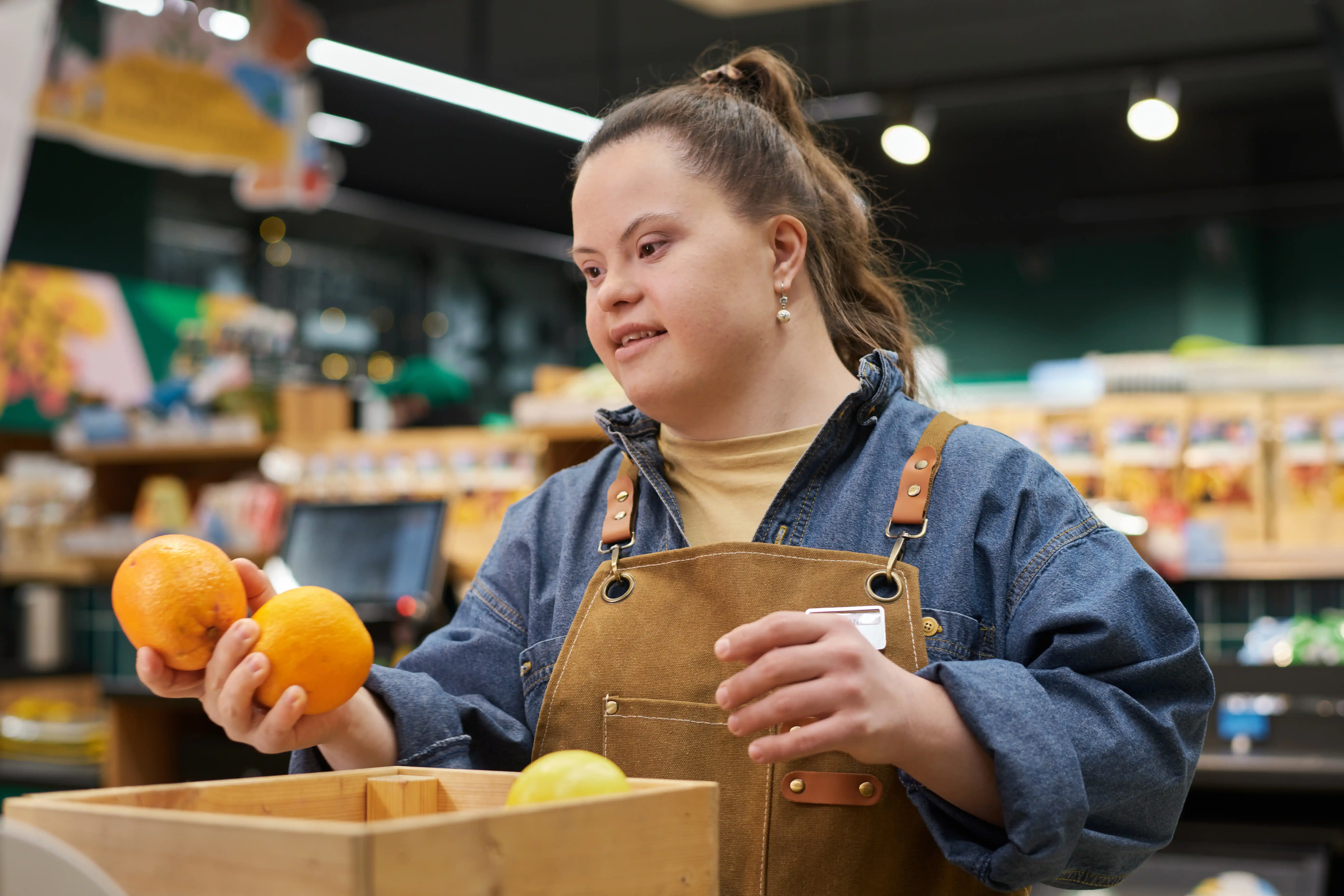 A retail grocery worker with Down syndrome wearing an apron while stocking produce, representing an employee entitled to a timely, good-faith interactive process and workplace accommodations under California FEHA