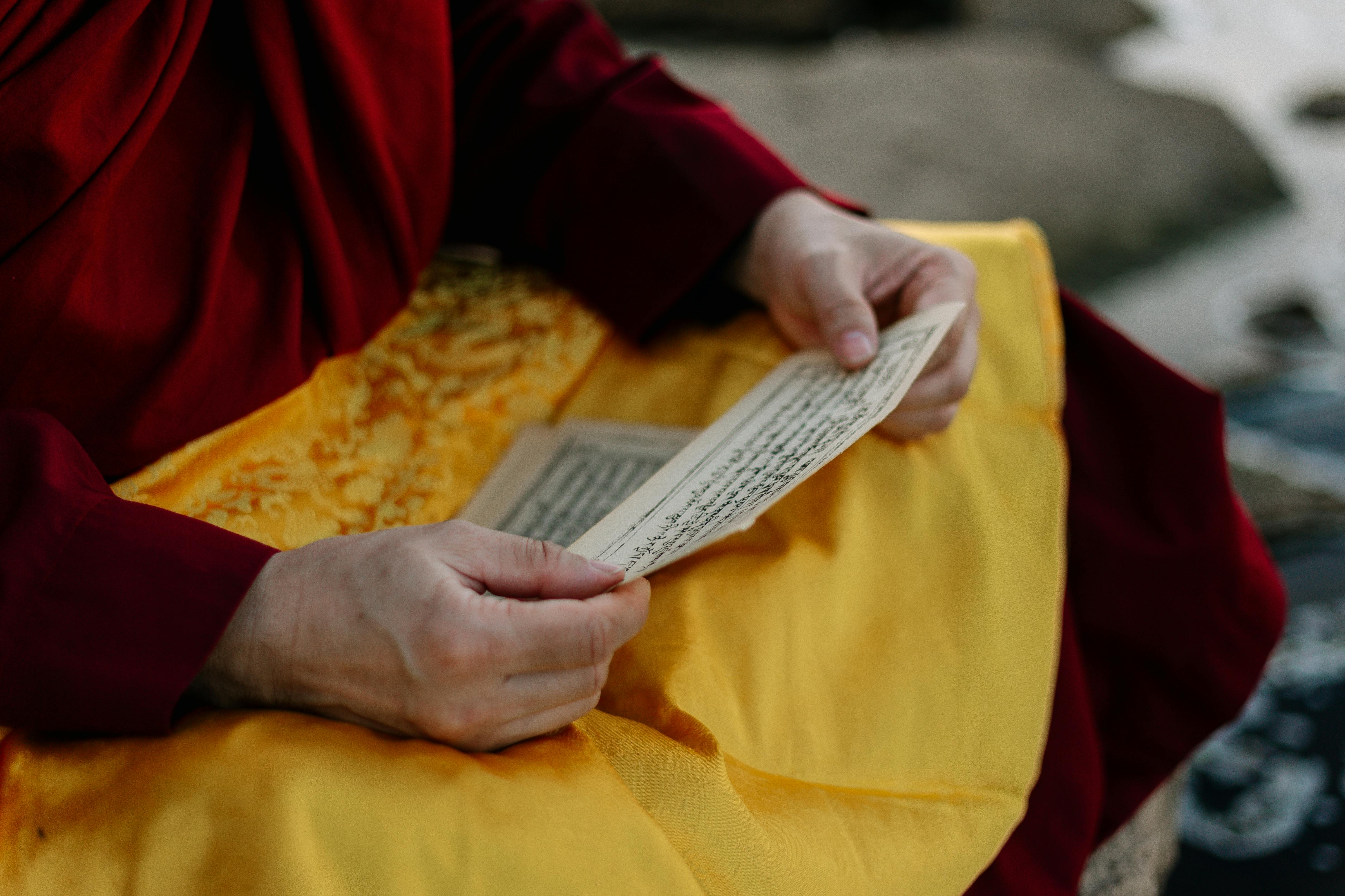 Mains d'un moine tenant un texte sacré en sanskrit sur fond de tissu jaune et rouge