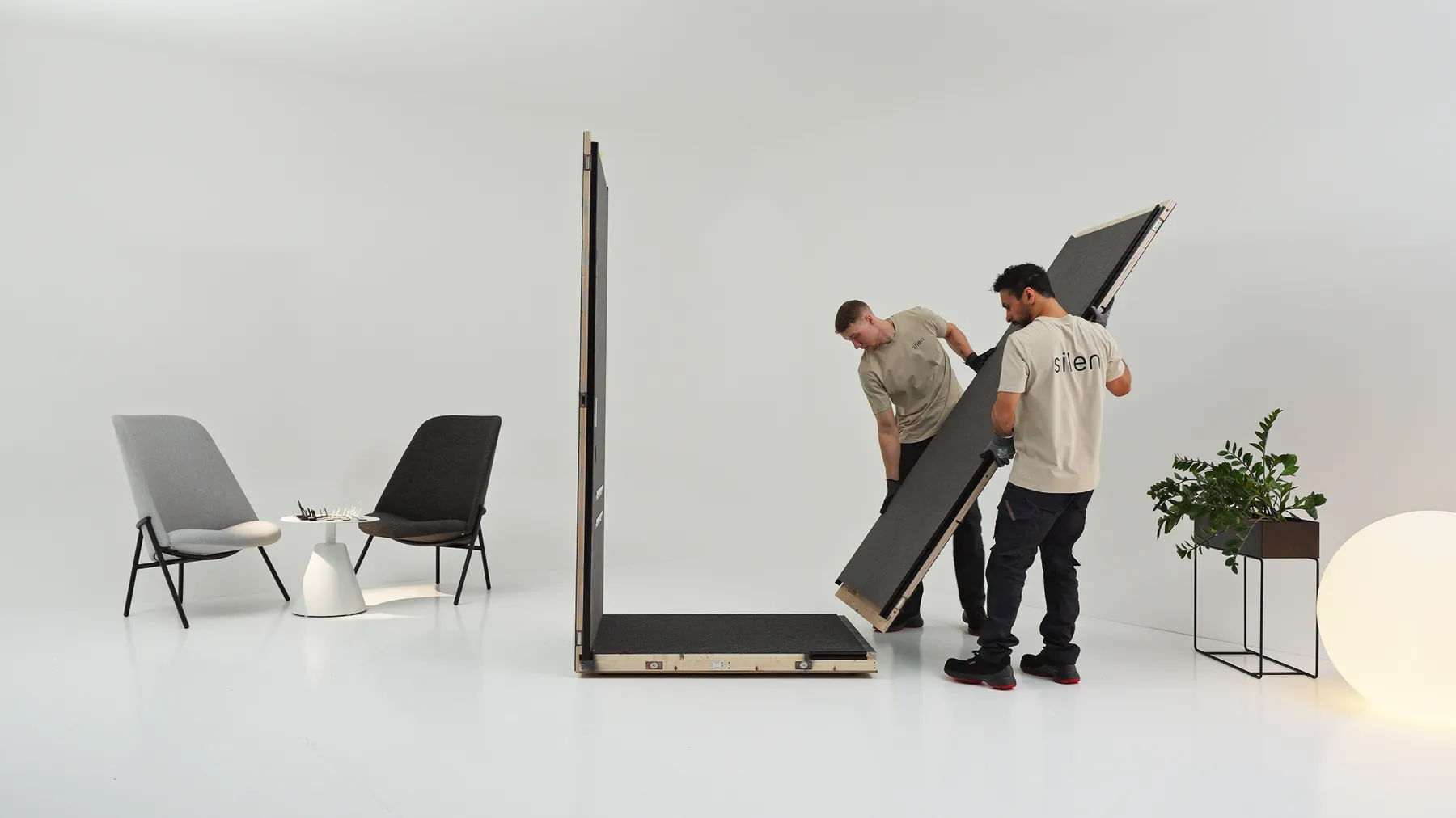Two Silen technicians carrying an assembled acoustic pod panel across a studio