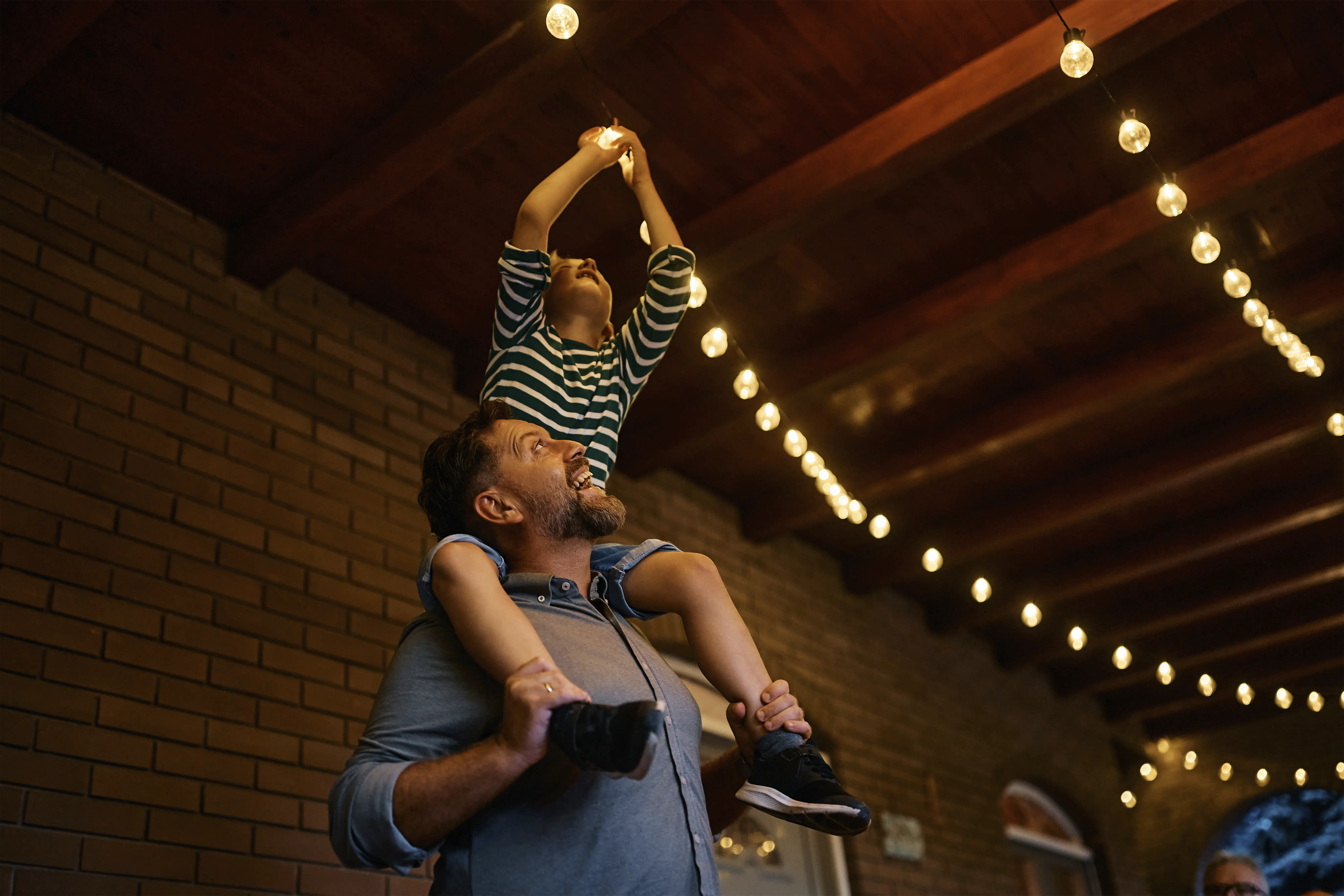 Man holding child on shoulders happily fixing an outdoor light bulb