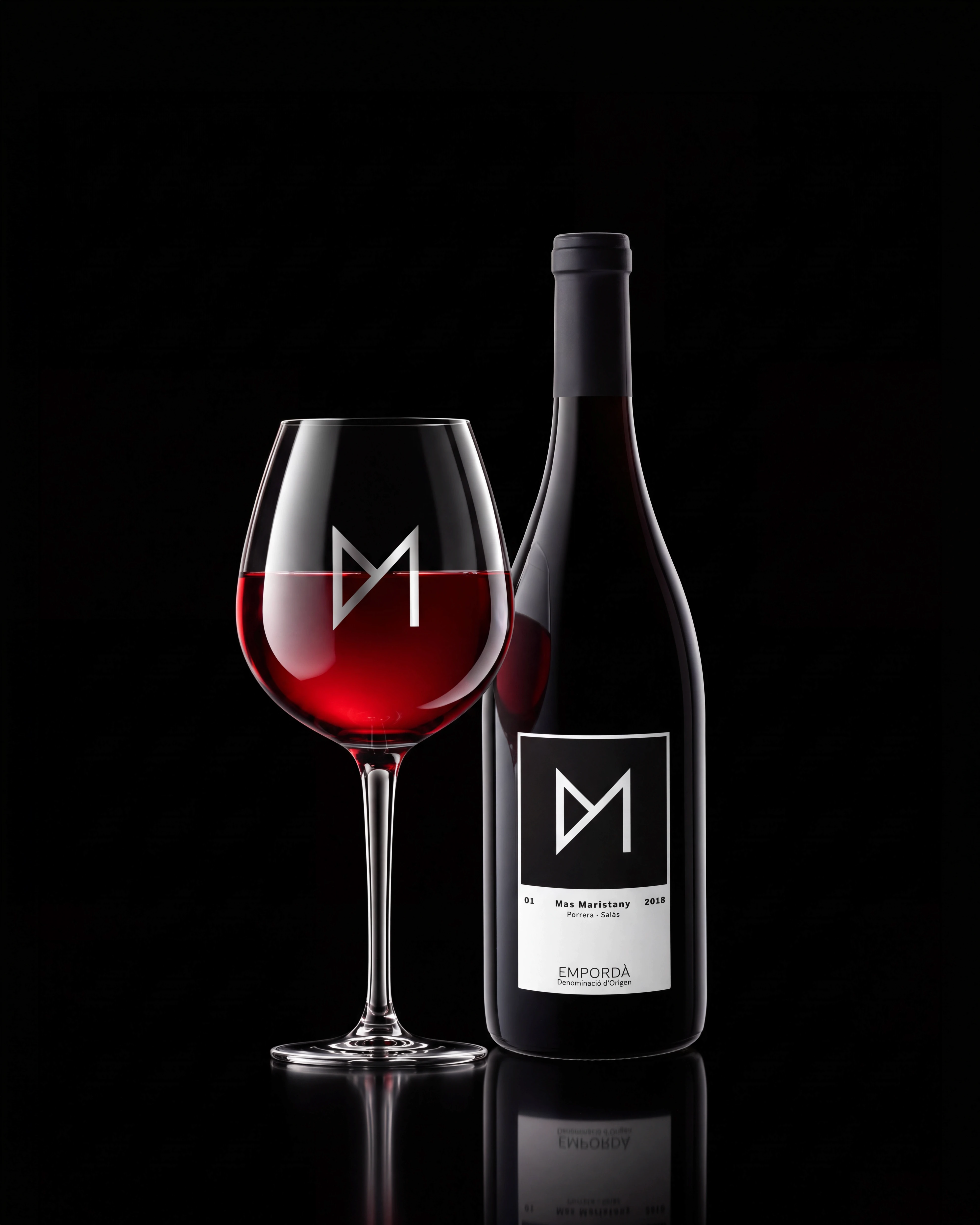 Glass of red wine beside a Mas Maristany bottle on a reflective black surface, brand identity design by Sebastian Saavedra