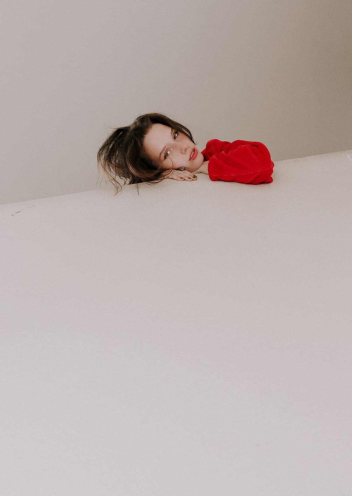 Model wearing red rests her head on a ledge for a creative shot at Revelator Studio in Shreveport.