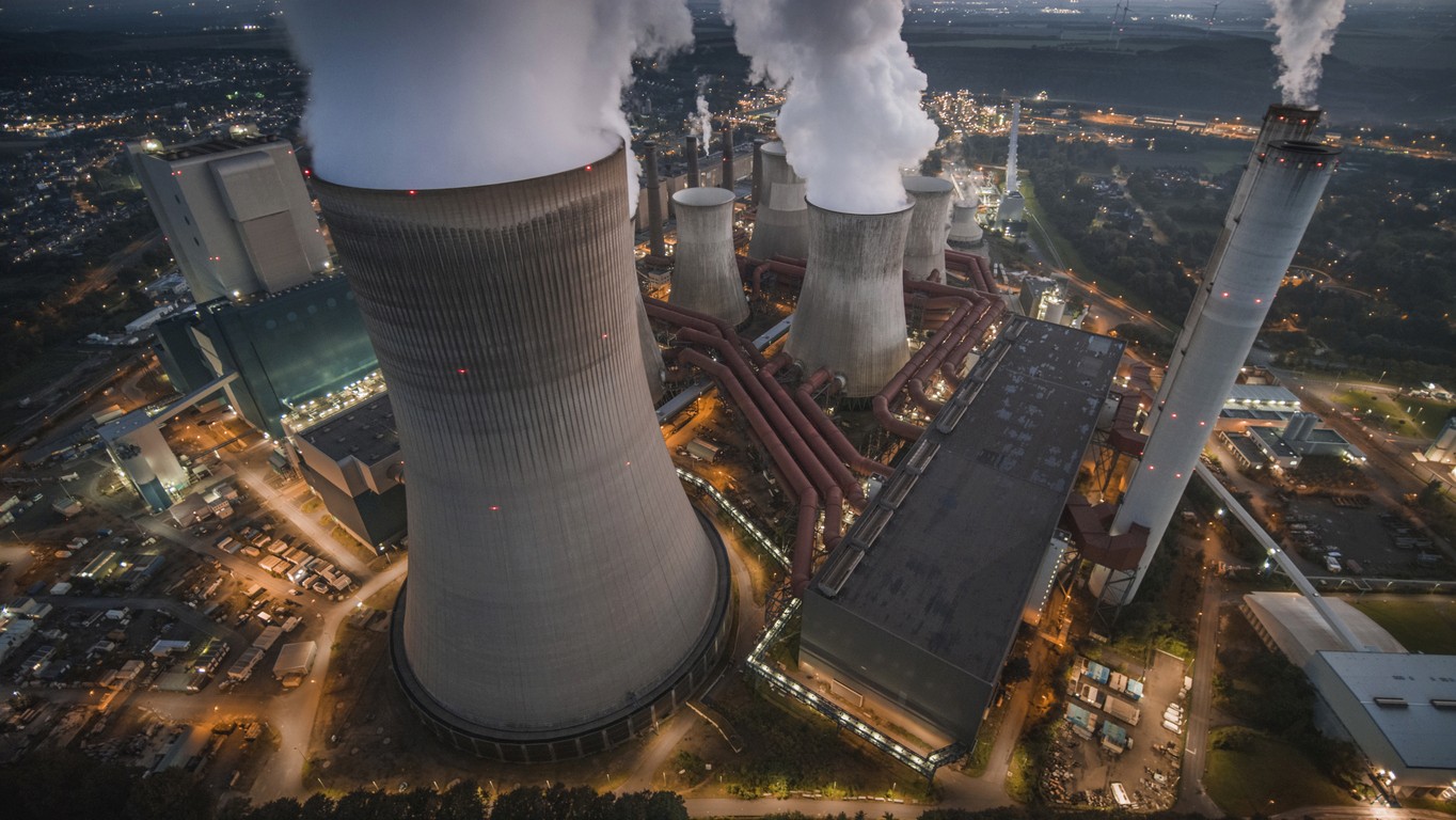 Aerial view of a coal fired power station with large cooling towers emitting co2 into the atmosphere. With its lights already turned on the power station is illuminated in moody twilight.