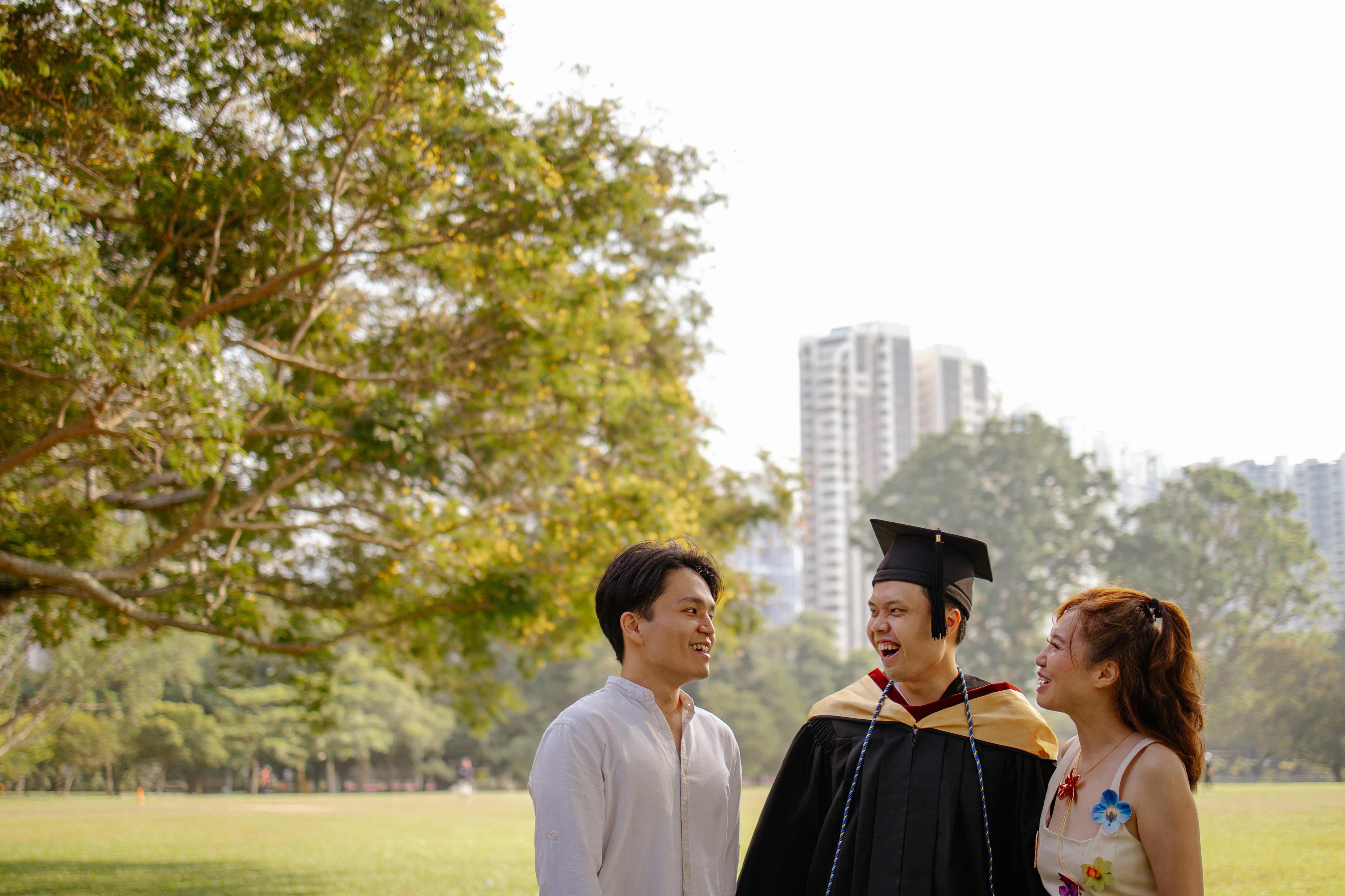 Graduate with his family standing under golden hour sunlight, trees in the background.
