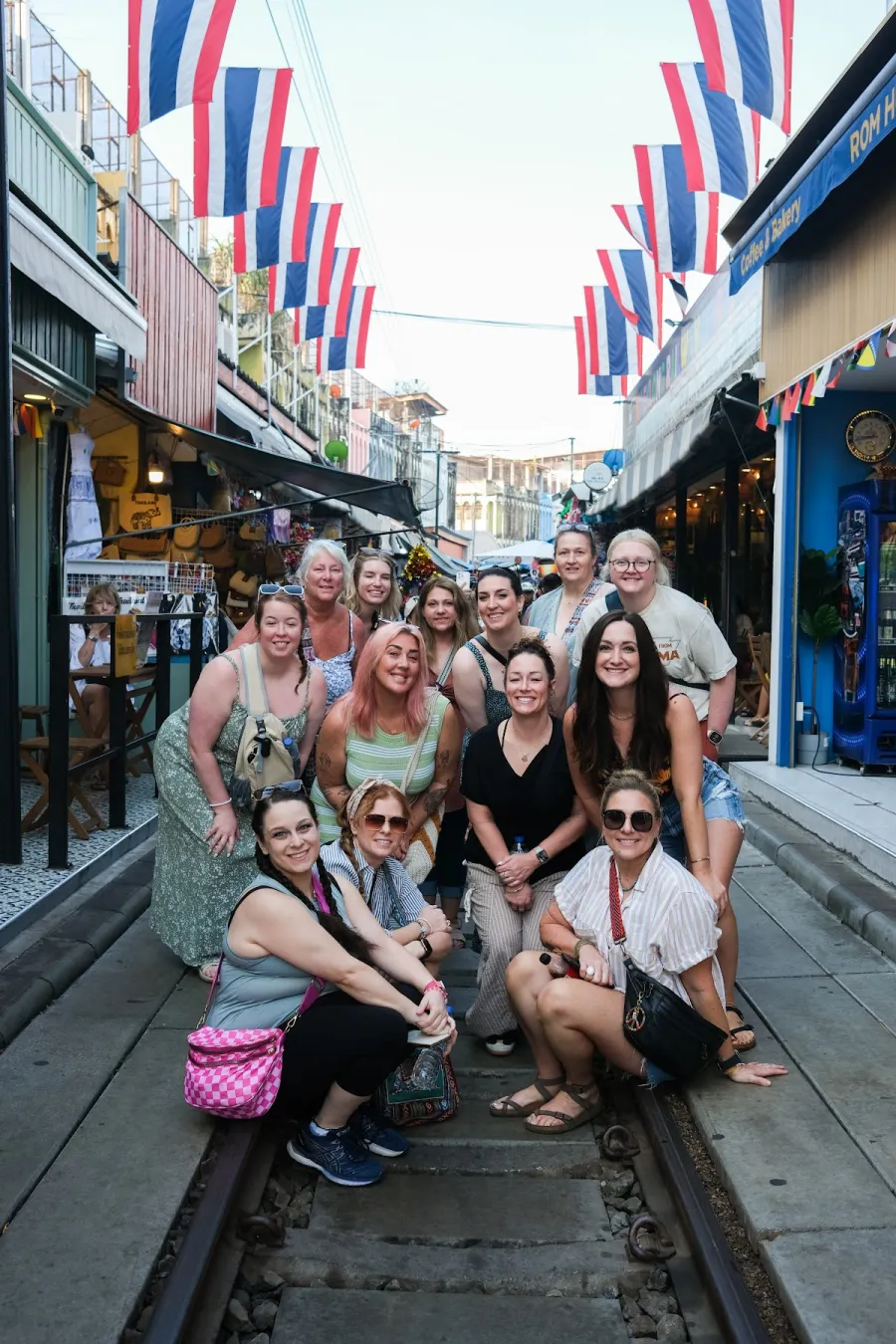 Group of women travelers posing on the railway tracks at Maeklong Railway Market in Bangkok, Thai flags overhead