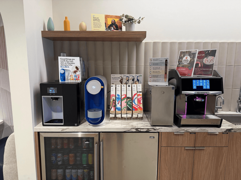 Title: BrewBird beside espresso equipment - Description: A BrewBird brewer placed between other office beverage equipment on a countertop.