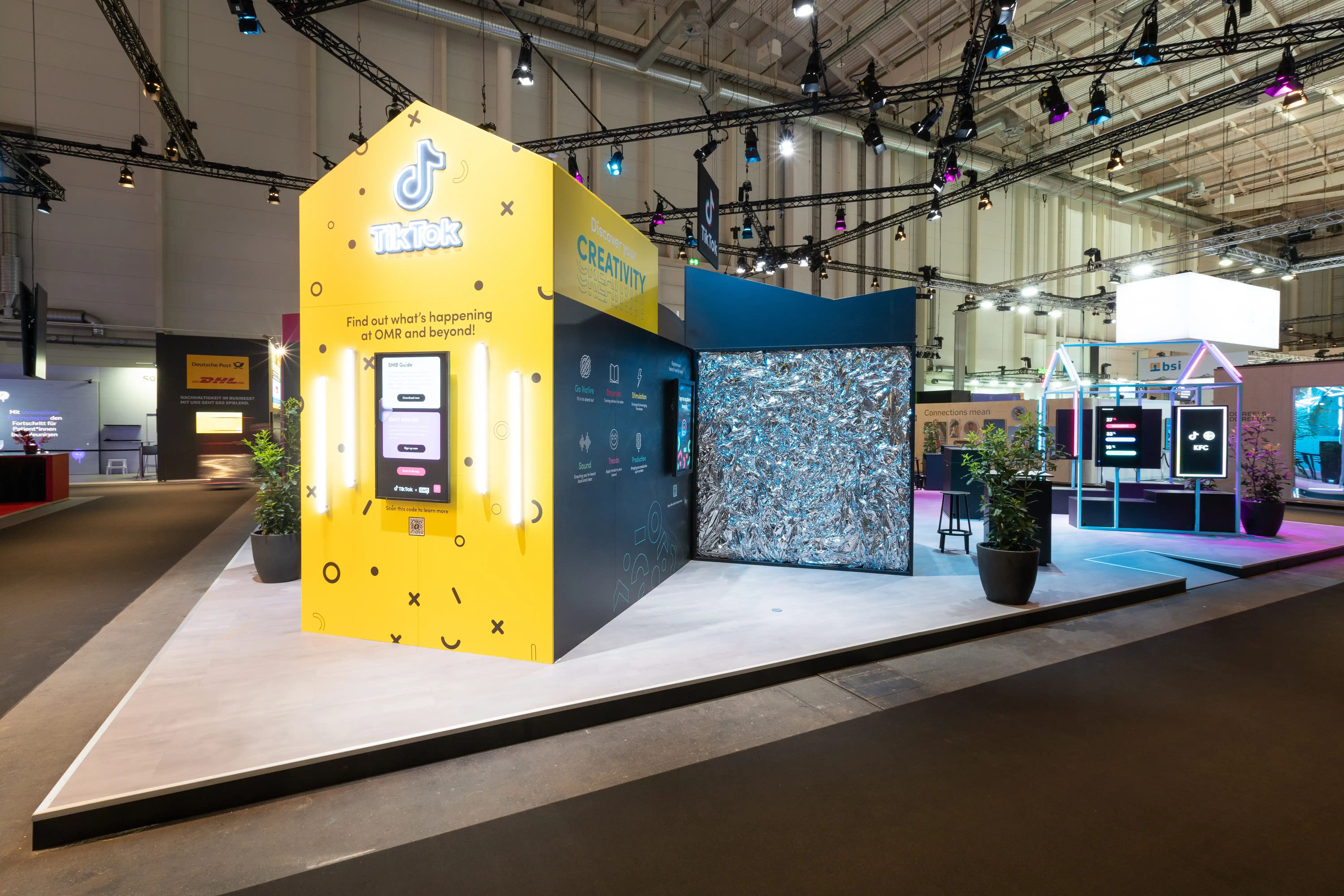 Side view of the TikTok booth with yellow info kiosk and a cube clad in crinkled silver foil.