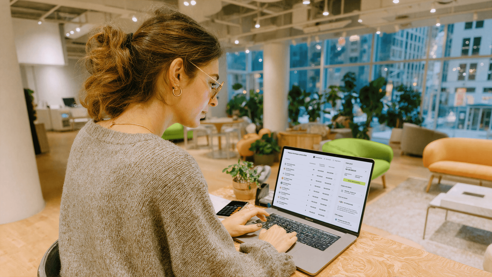 Mulher de óculos trabalhando em um notebook em uma clínica, com o painel financeiro da Tivita aberto na tela para conciliação bancária em tempo real