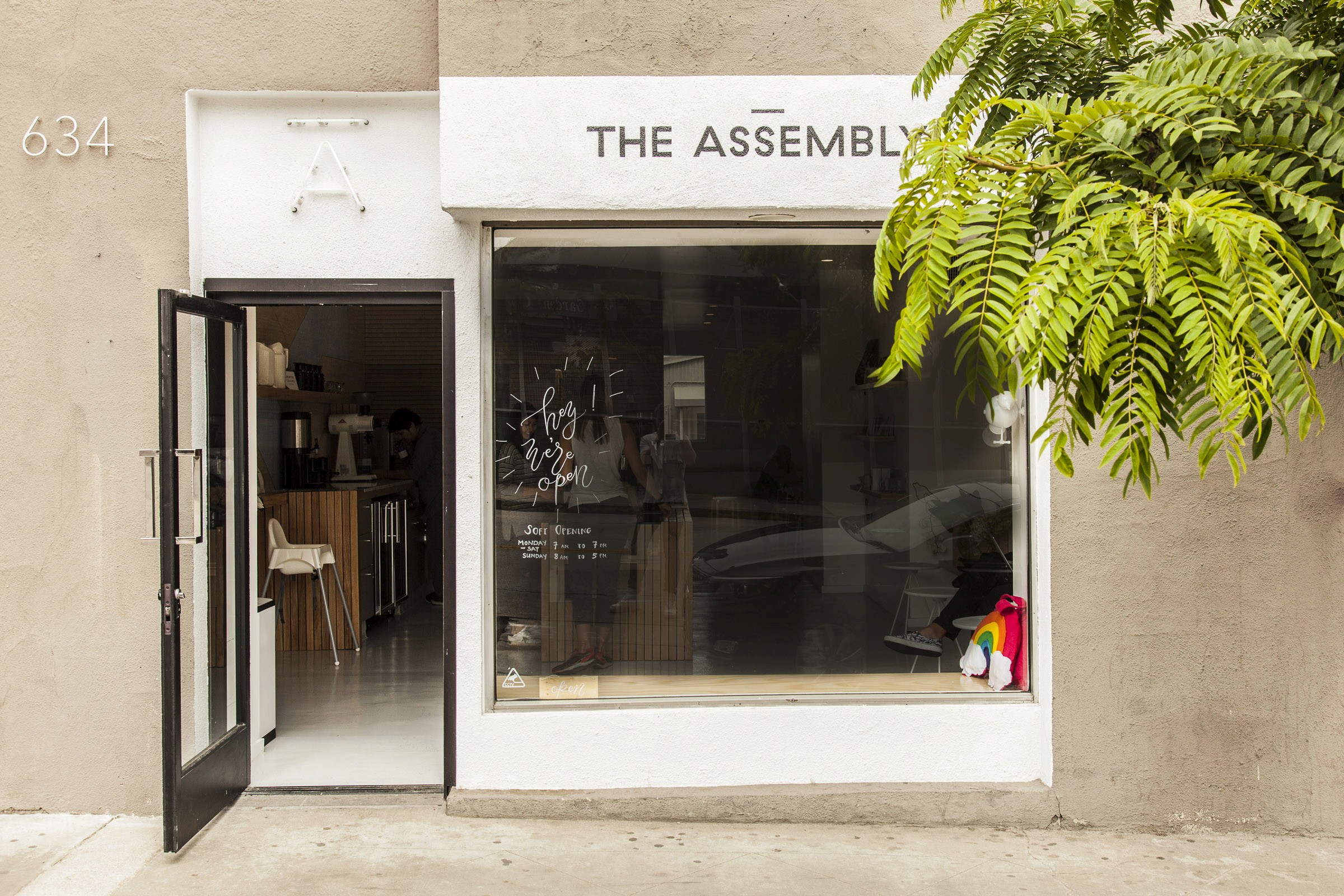 The Assembly storefront with open glazed door, simple wordmark and hanging fern.