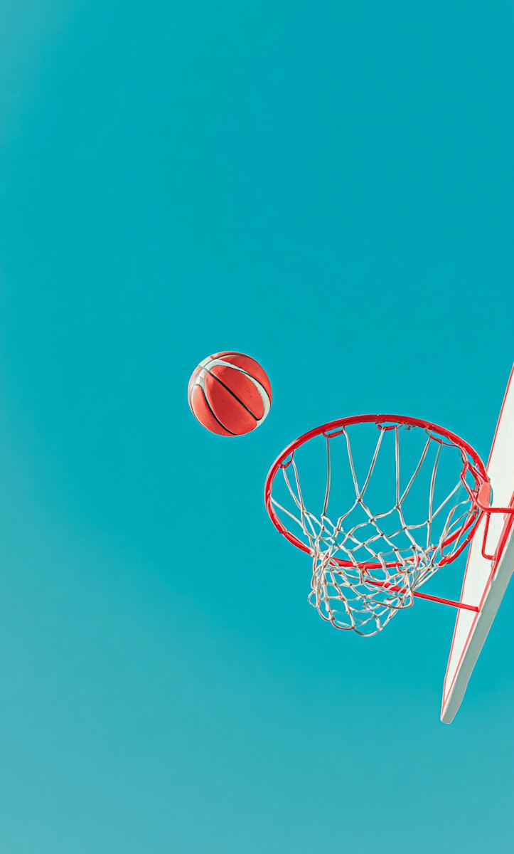 A basketball in motion toward a hoop against a vivid blue sky. Simple, clear, and dynamic with vibrant colors.