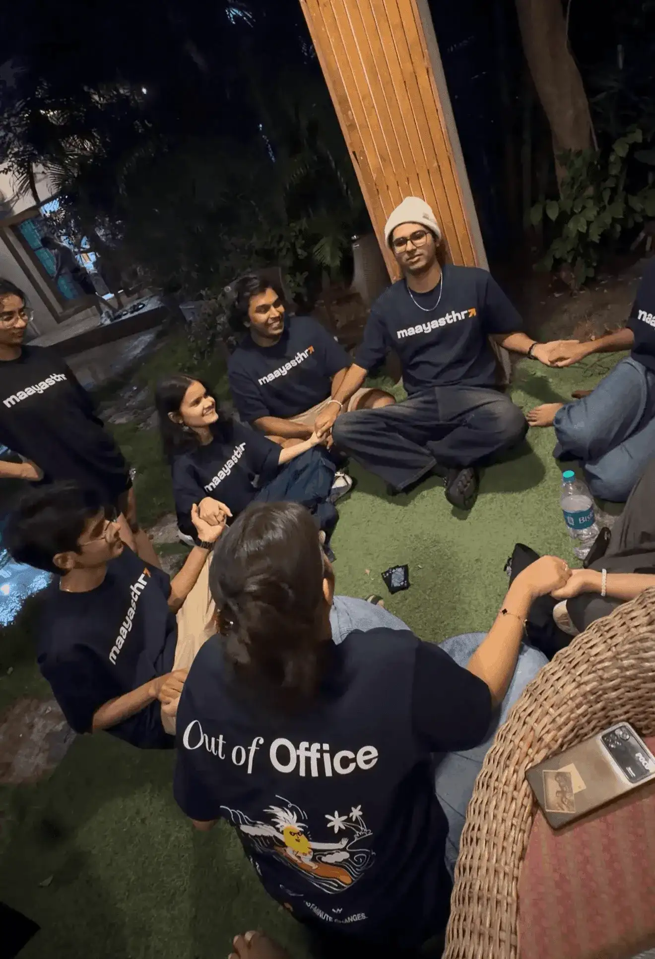 Maayasthra team sitting in a circle outdoors at night, engaging in a group activity during an out-of-office event.