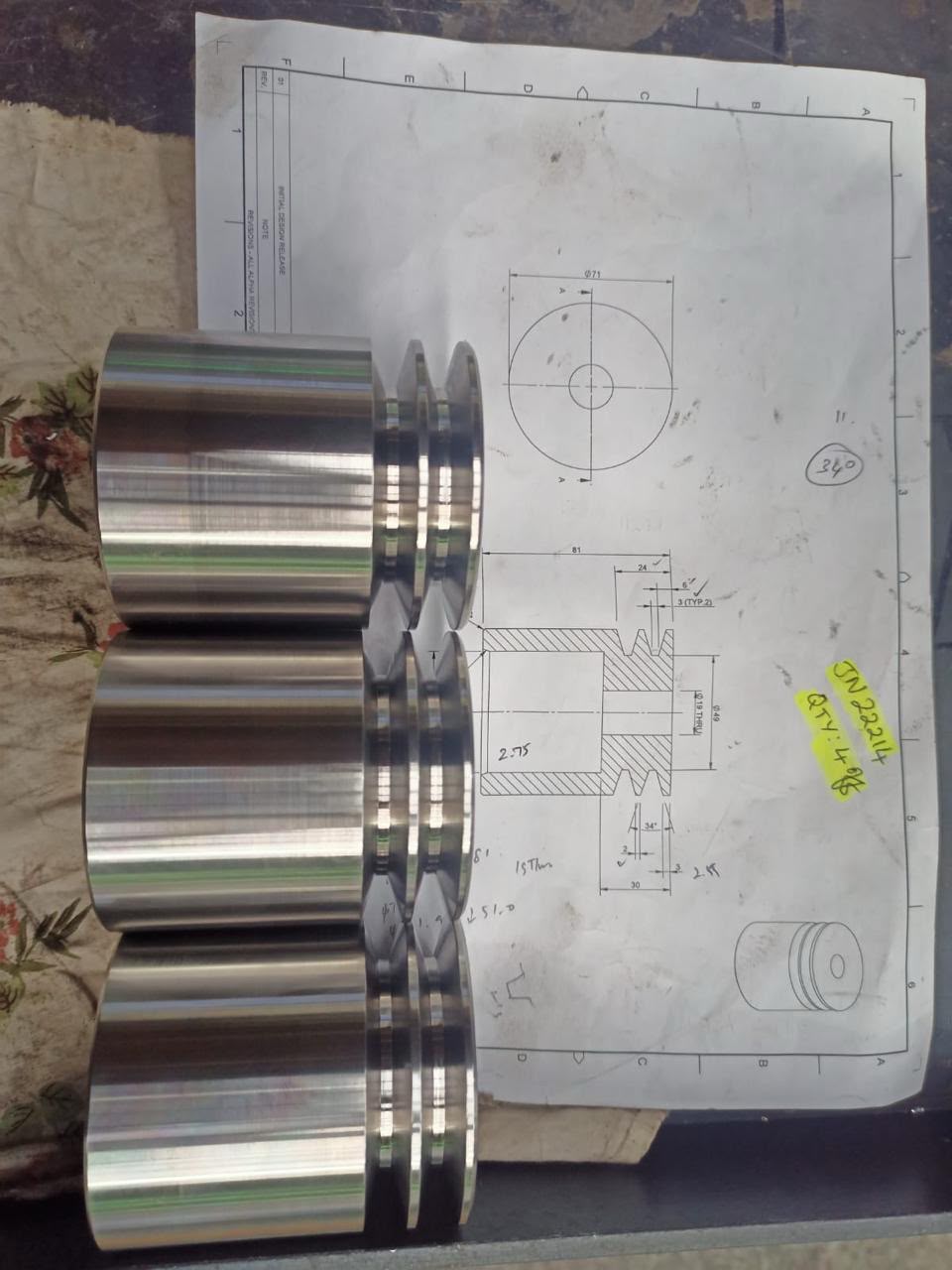 Precision machined metal pulley components placed on their corresponding technical drawing.
