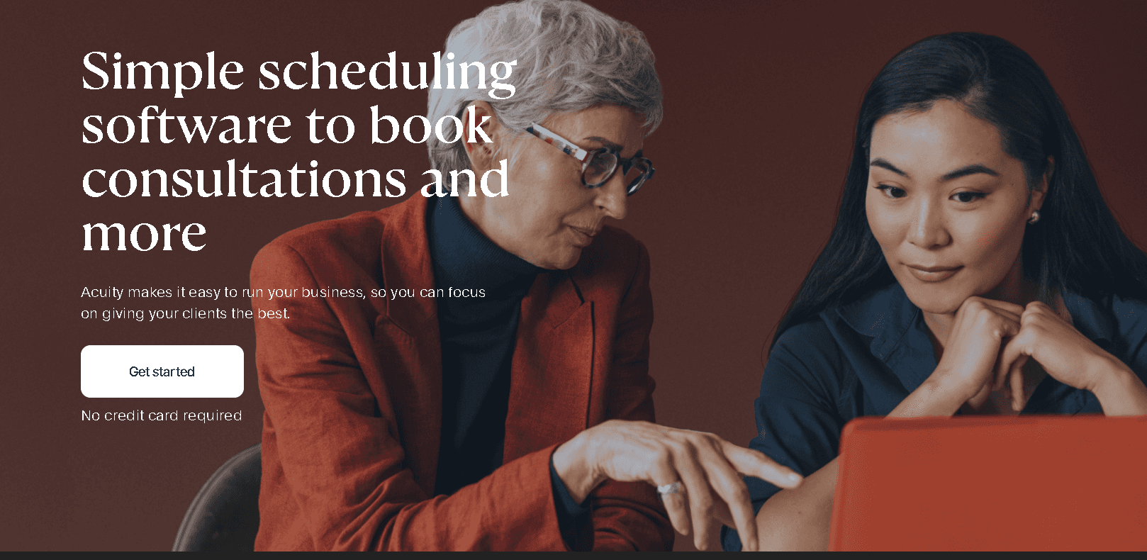 Two professional women collaborating over a laptop while looking at the Acuity Scheduling page to compare pricing and features.