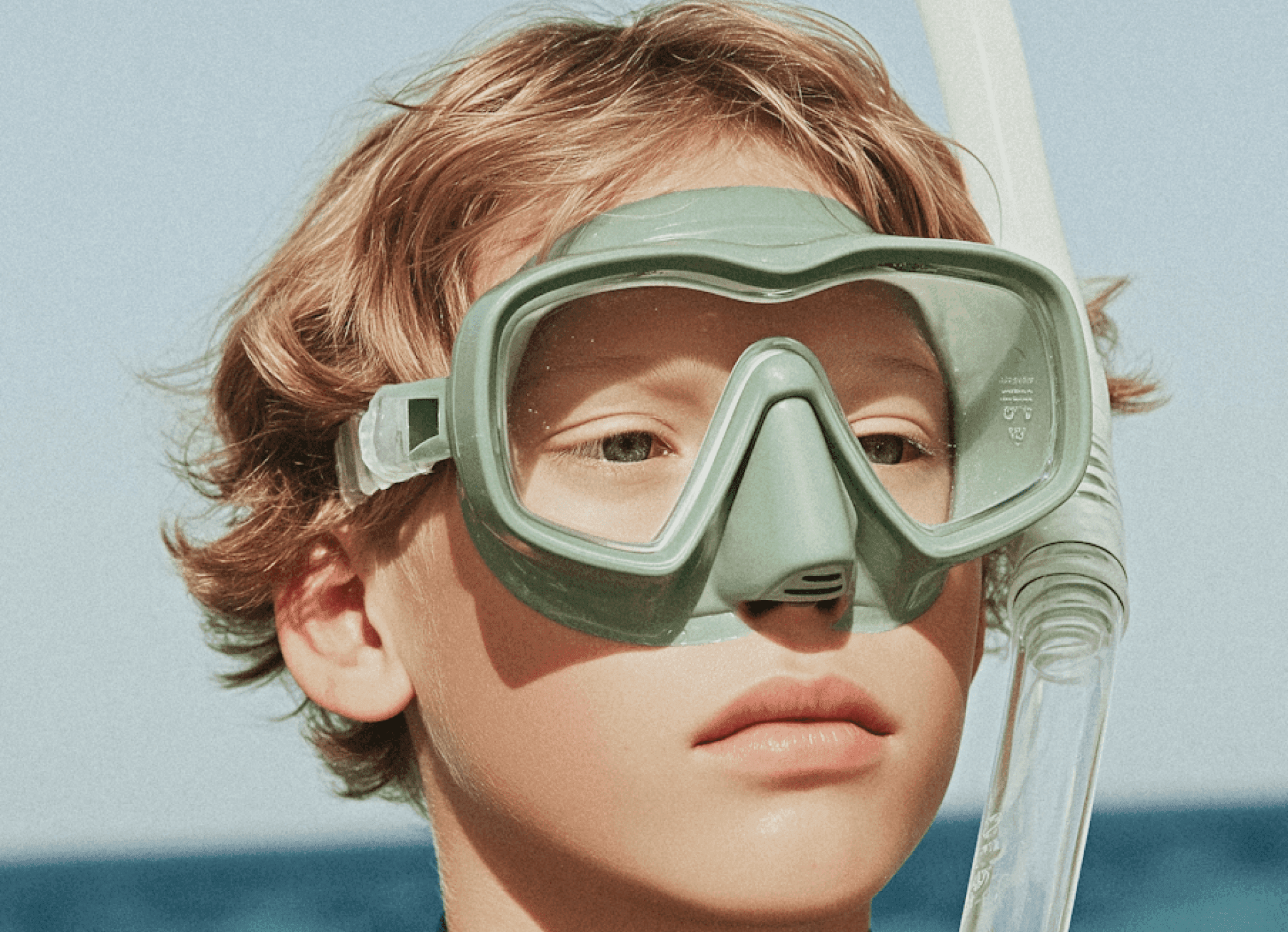 Child wearing a snorkel mask, ready for underwater exploration by the sea.