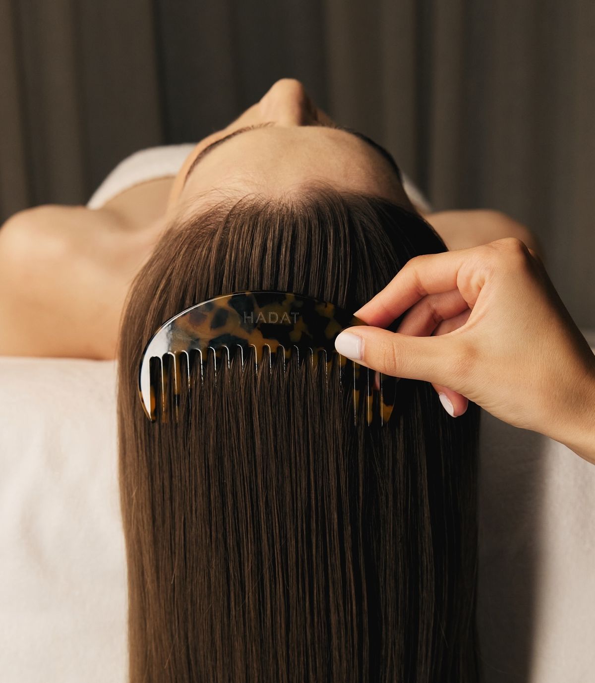 A close-up of four smooth black hot stones neatly stacked on a white massage table. The warm sunlight reflects off the stones, creating a soothing and tranquil spa atmosphere.