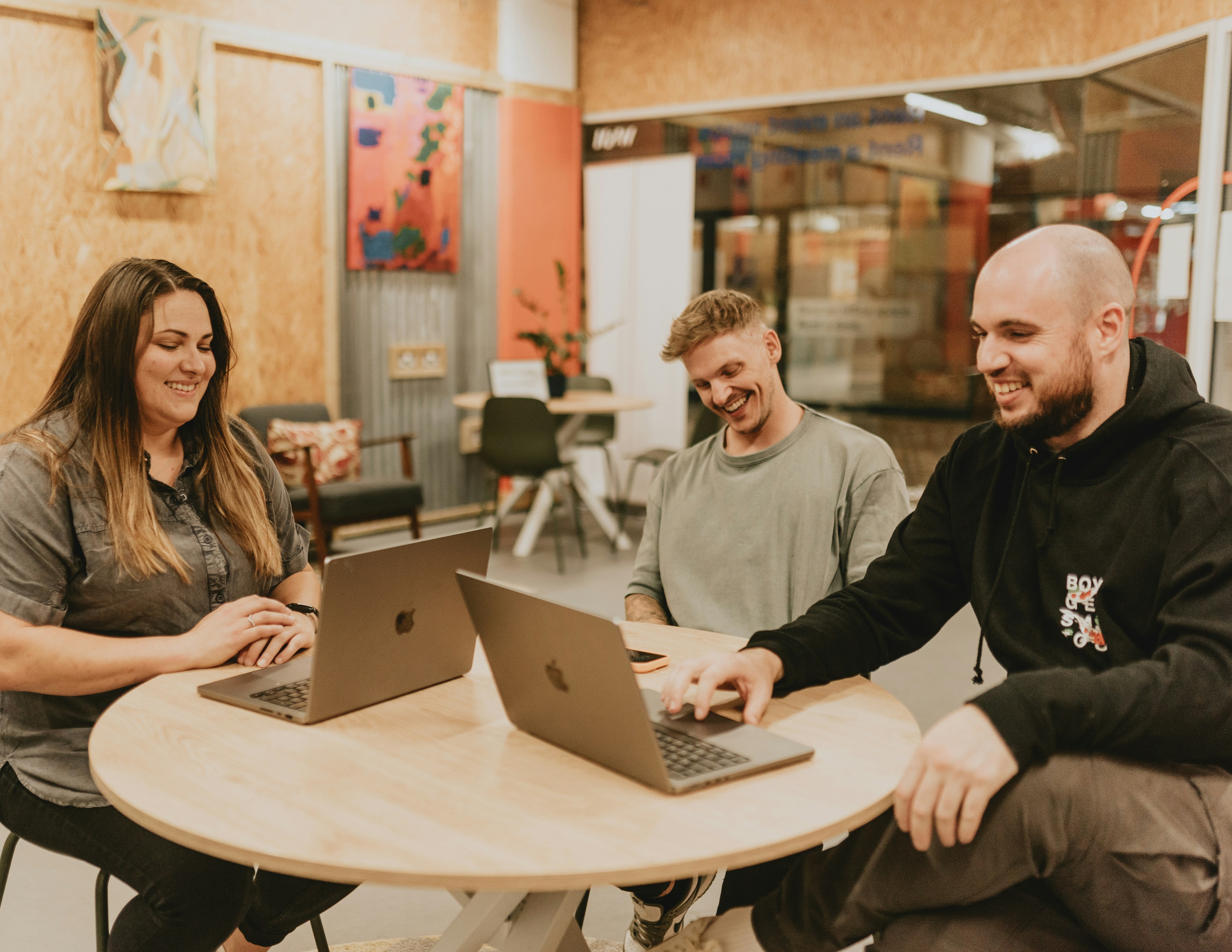 Three people collaborate around a table with laptops.