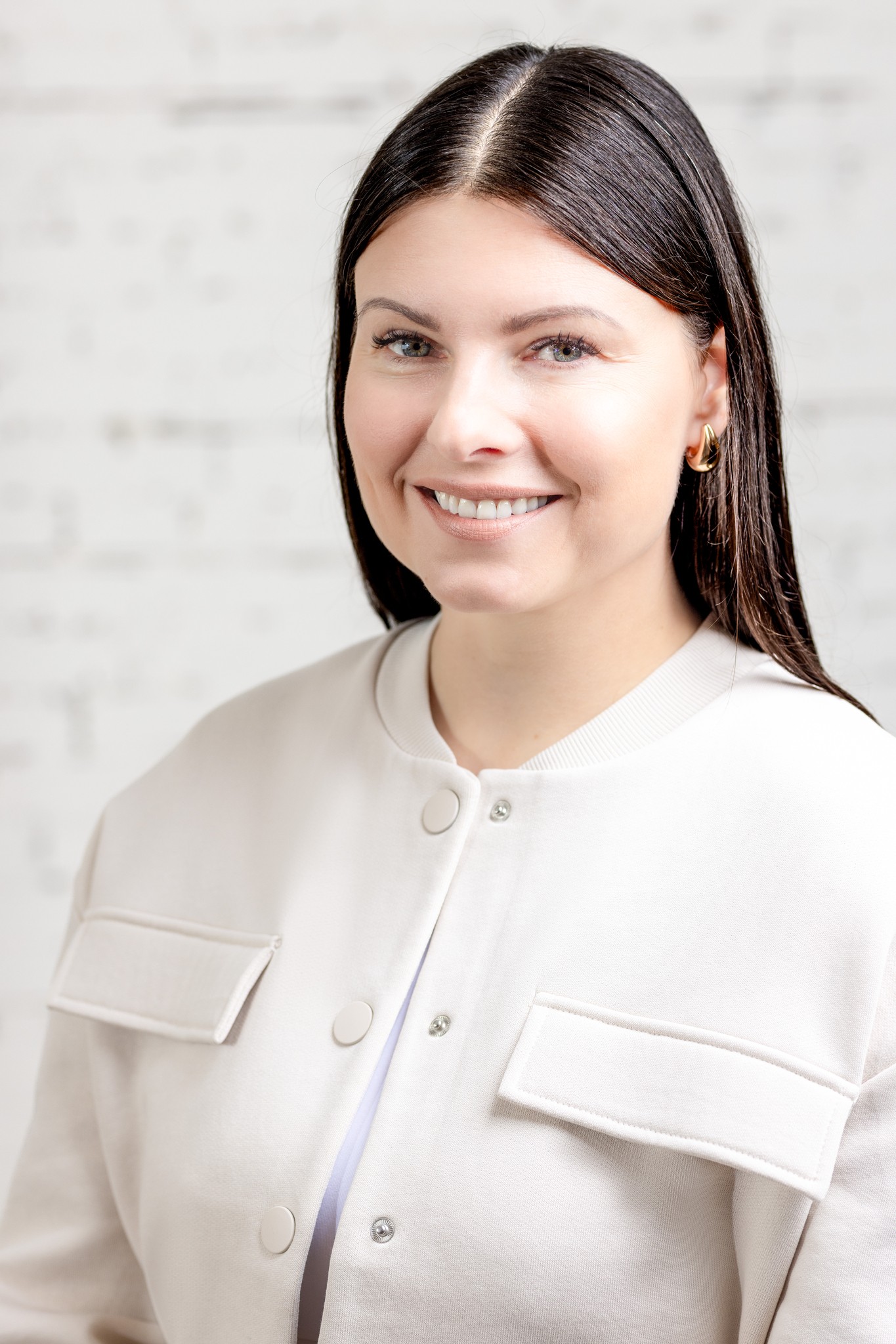 Image of Woman in black dress standing in front of white brick wall with a warm gentle smile.