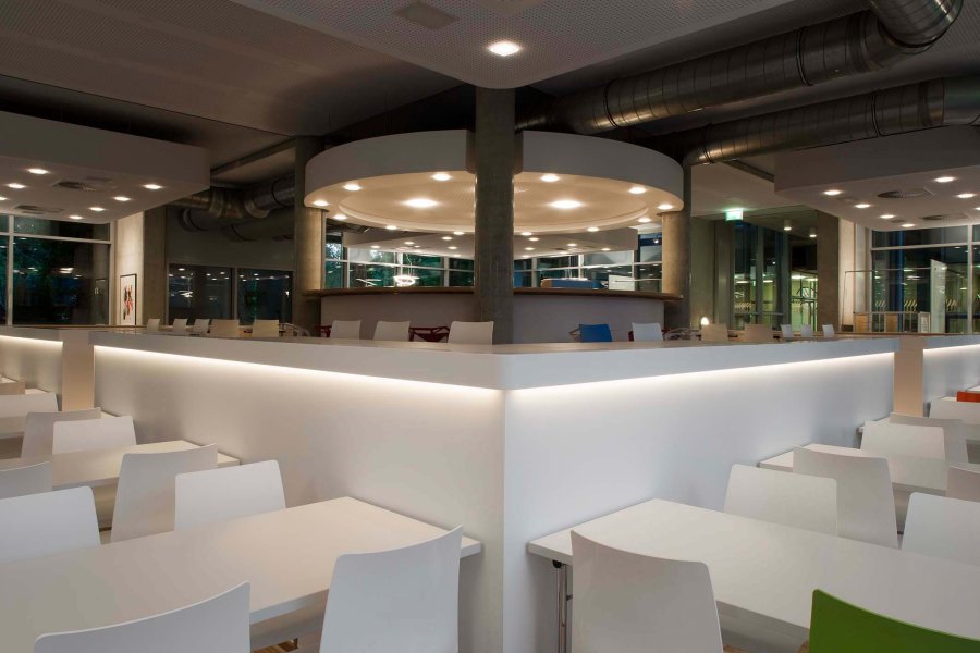 Moderne Kantine mit weißem Interieur und Lichtdesign. Sitzbereiche und Bar.