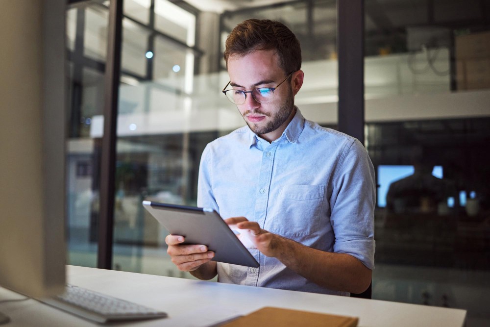 Man wearing glasses using a tablet in a modern office, representing organised digital document control and contractor record storage.