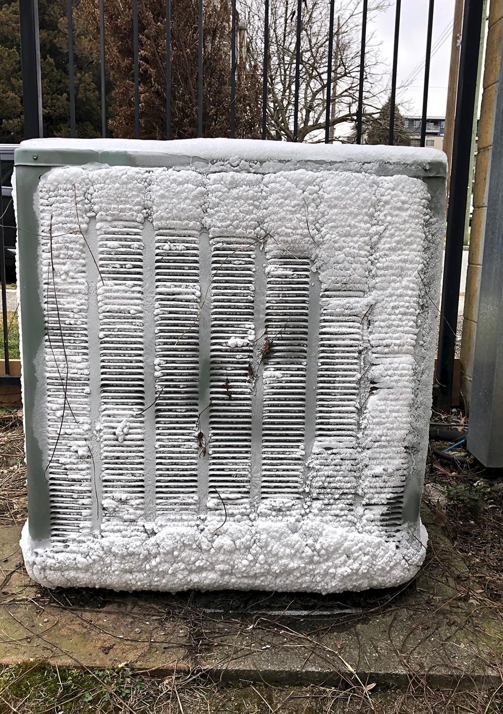 Air source heat pump unit outside a UK home with frost on external pipework due to uninsulated underground pipe runs and poor system design
