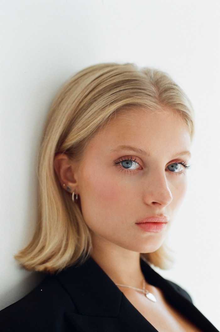 Portrait of a woman with blonde hair, wearing a black blazer, against a plain white background. She looks directly at the camera.
