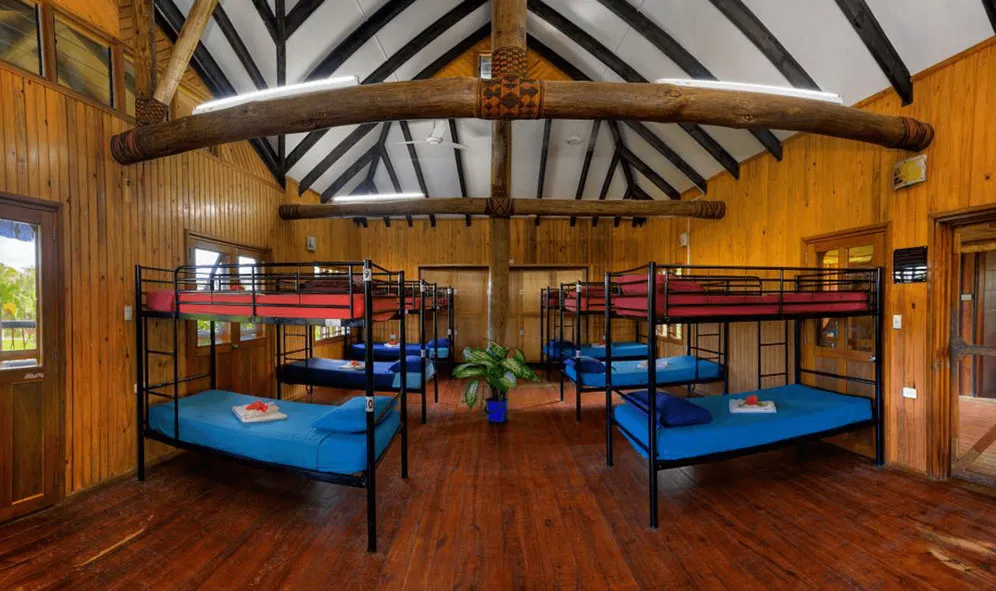 Large dormitory room at Uprising Beach Resort with multiple bunk beds, wooden walls, and a high-beamed ceiling.