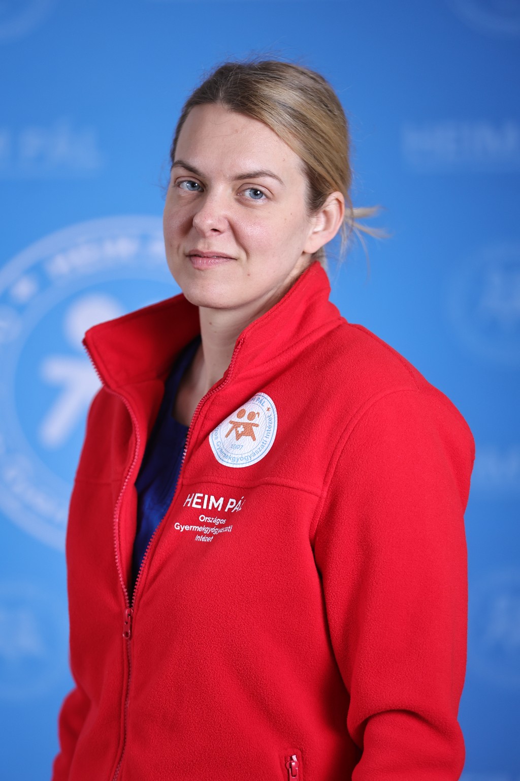 Szőke összefogott hajú nő piros kardigánban