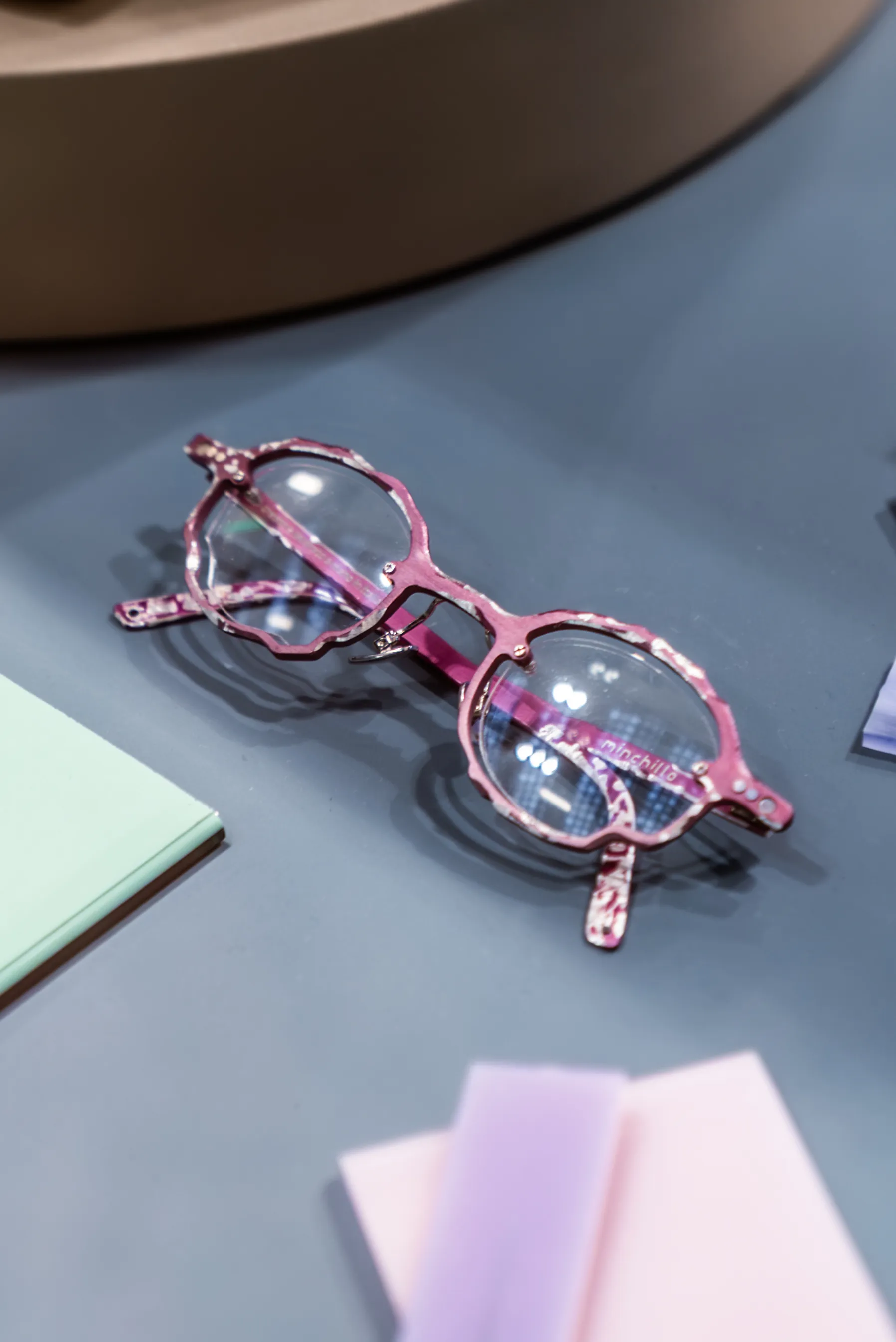 Occhiale IDIA associato a Laura, con montatura originale dalle tonalità rosa e traslucide fotografata all’interno di una composizione editoriale. La fotografia racconta uno dei risultati del percorso IDIA di Ottica Dentella ad Ancona, in cui ogni occhiale viene progettato individualmente attraverso studio del viso, colori, proporzioni e caratteristiche personali.