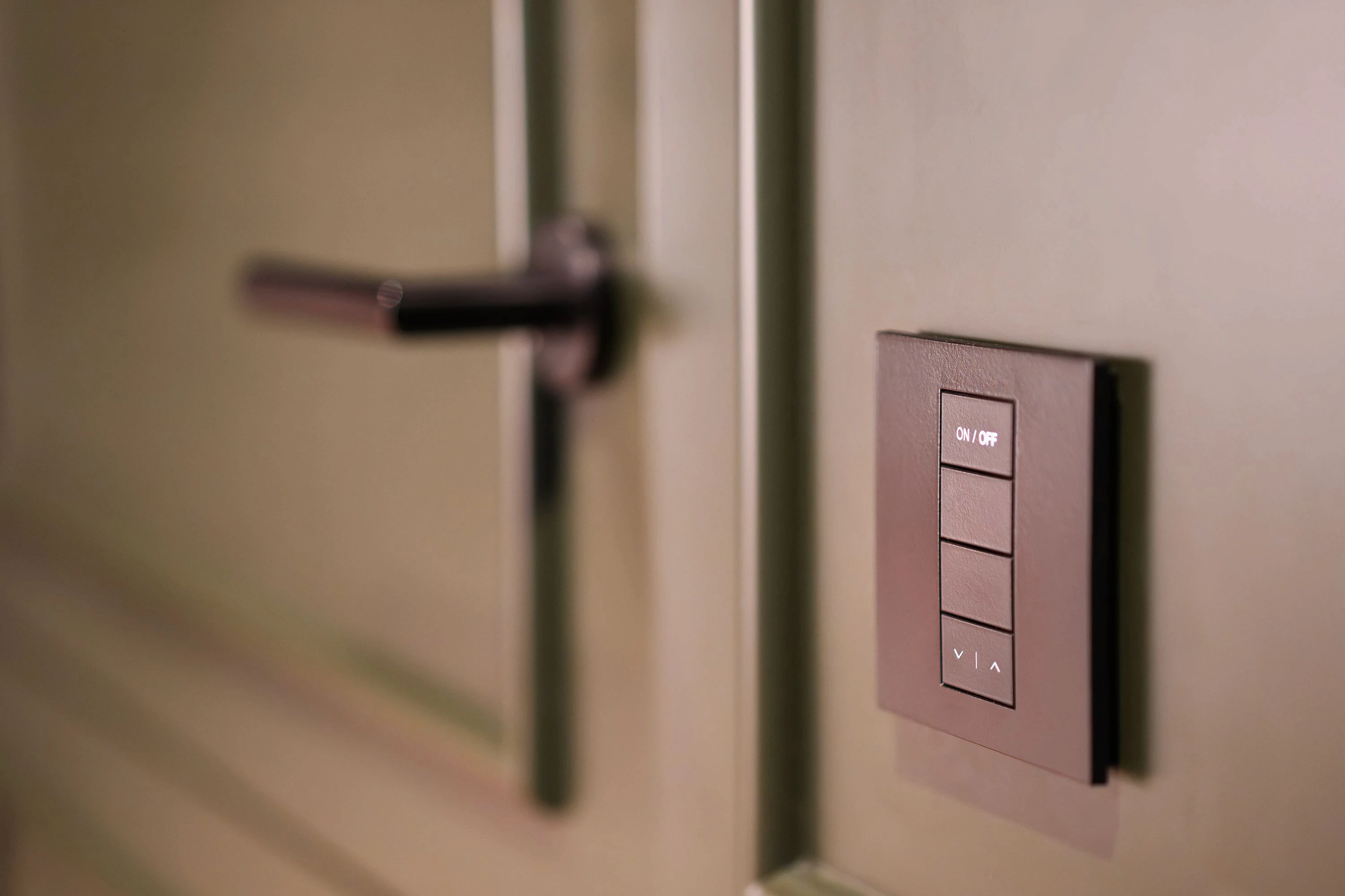 Close-up of a modern matte black smart light switch with an integrated dimmer control next to a door.