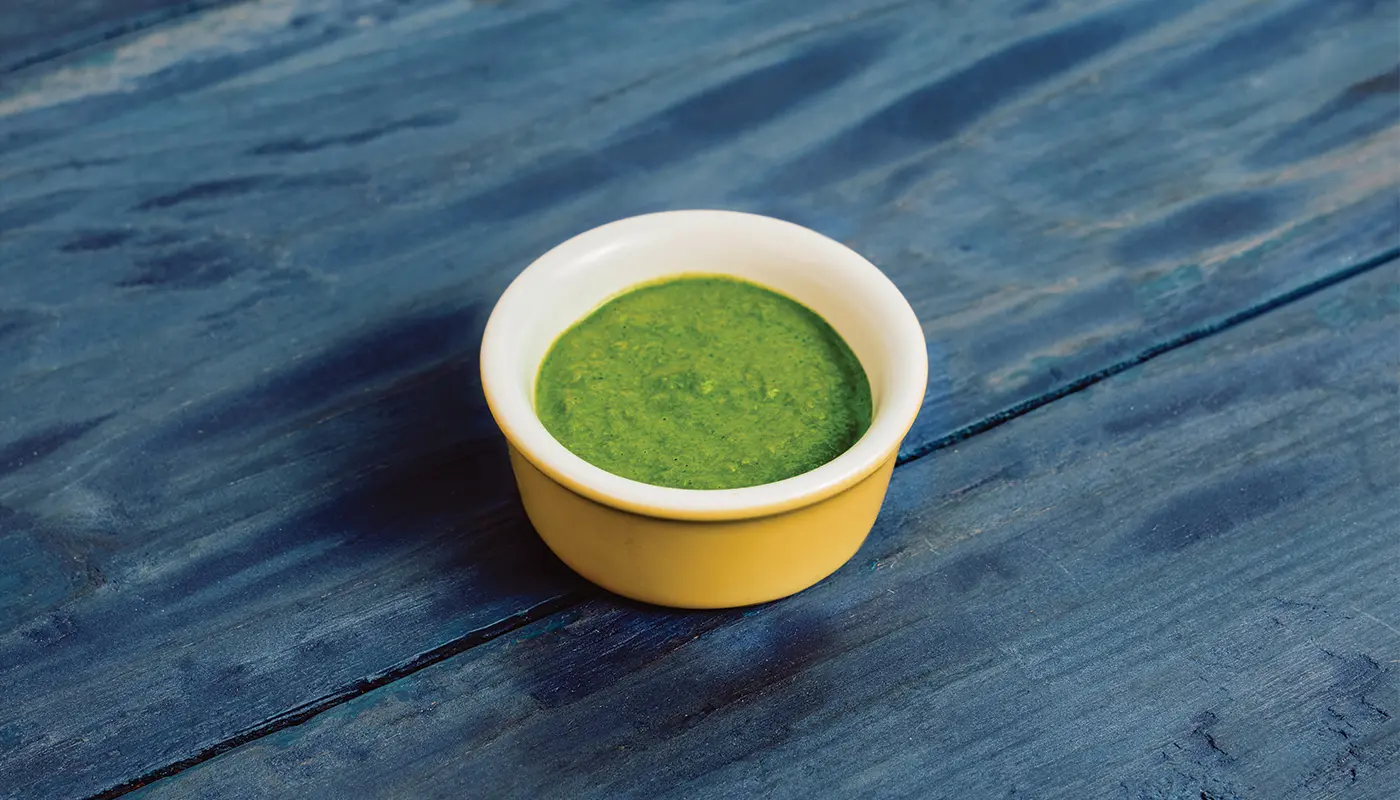 Island Herb Sauce in a small yellow dish on blue wooden boards.