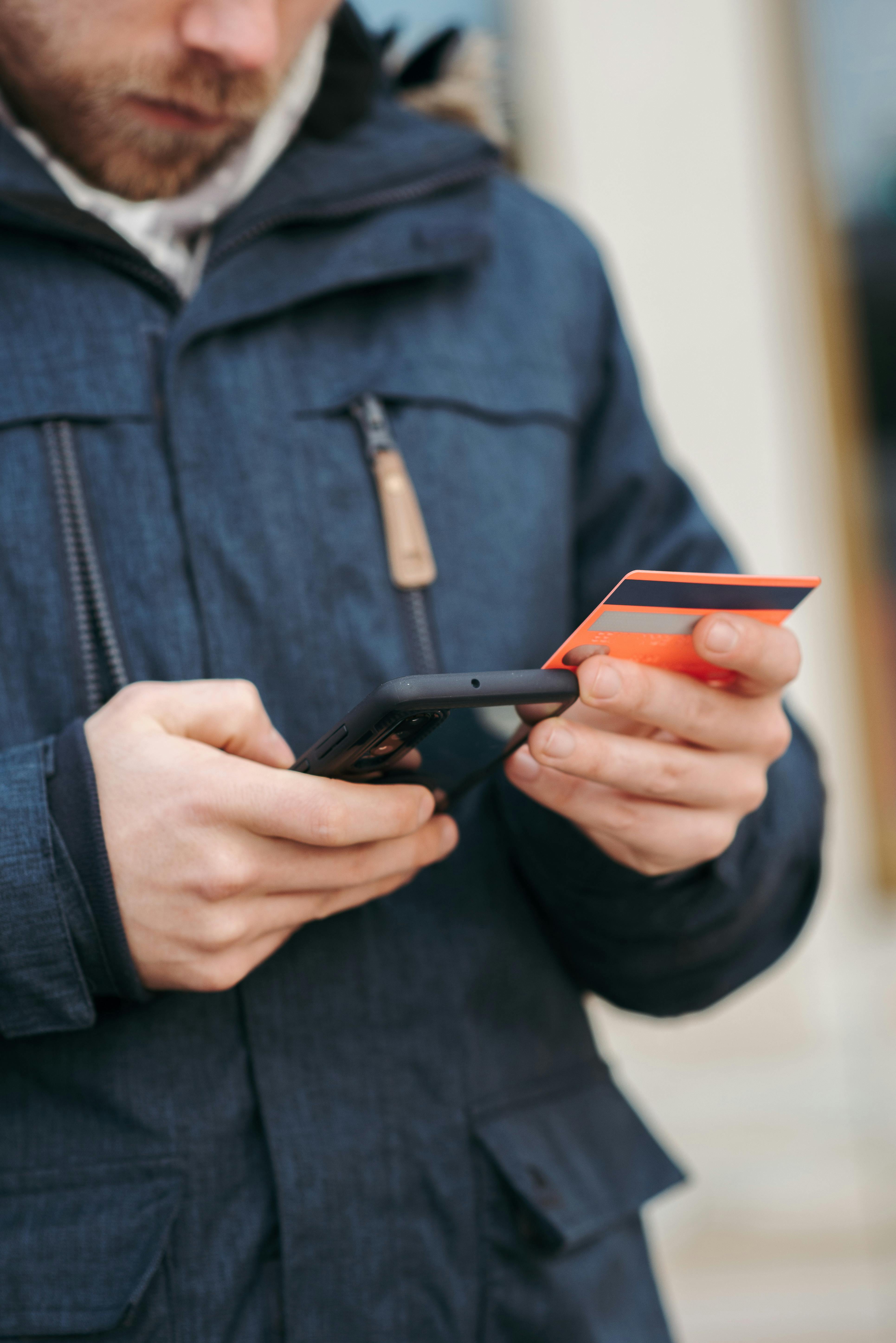 Person holding a smartphone in one hand and a credit card in the other, appearing to make an online purchase on a mobile device.