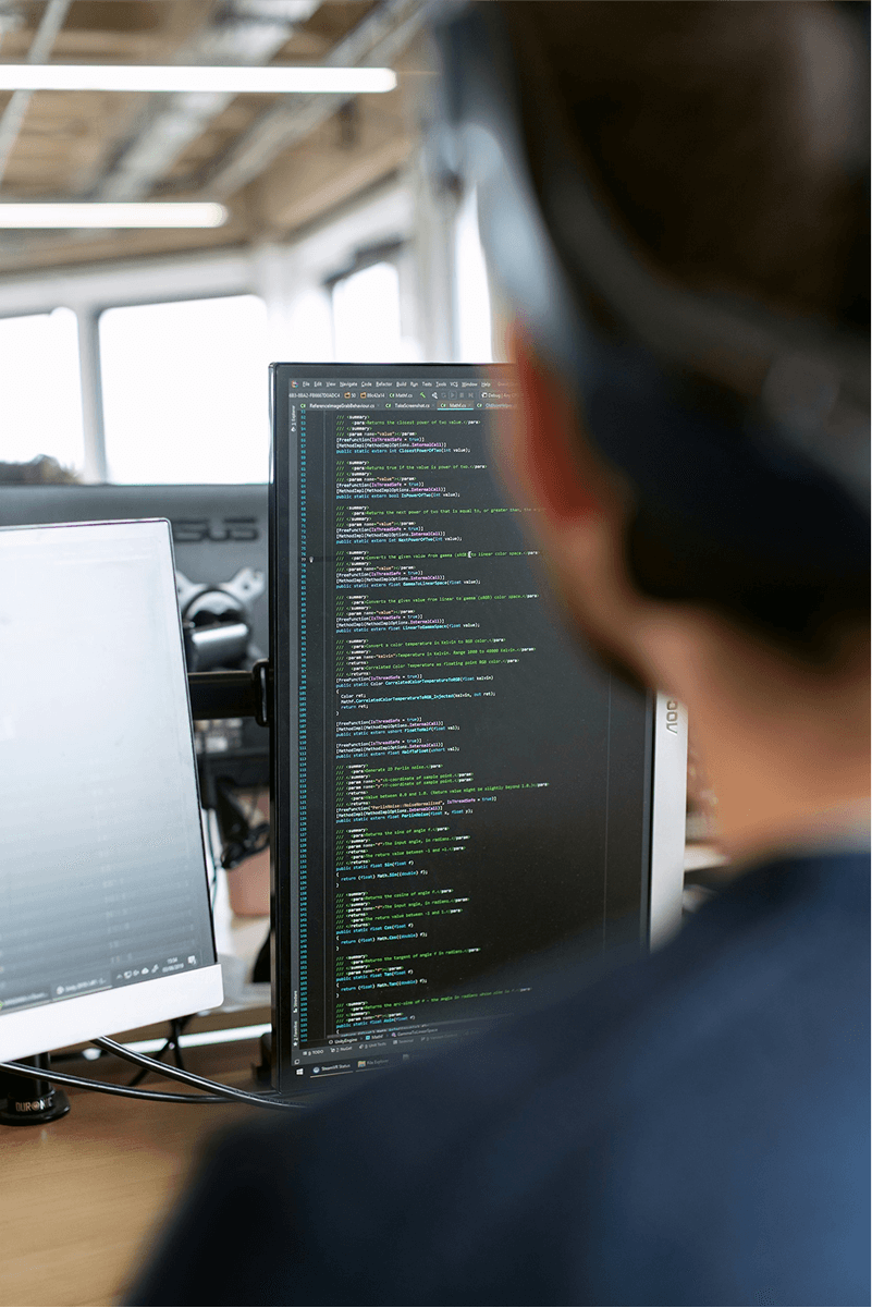 Person seated at a desk working with source code displayed on dual monitors in a professional office environment.