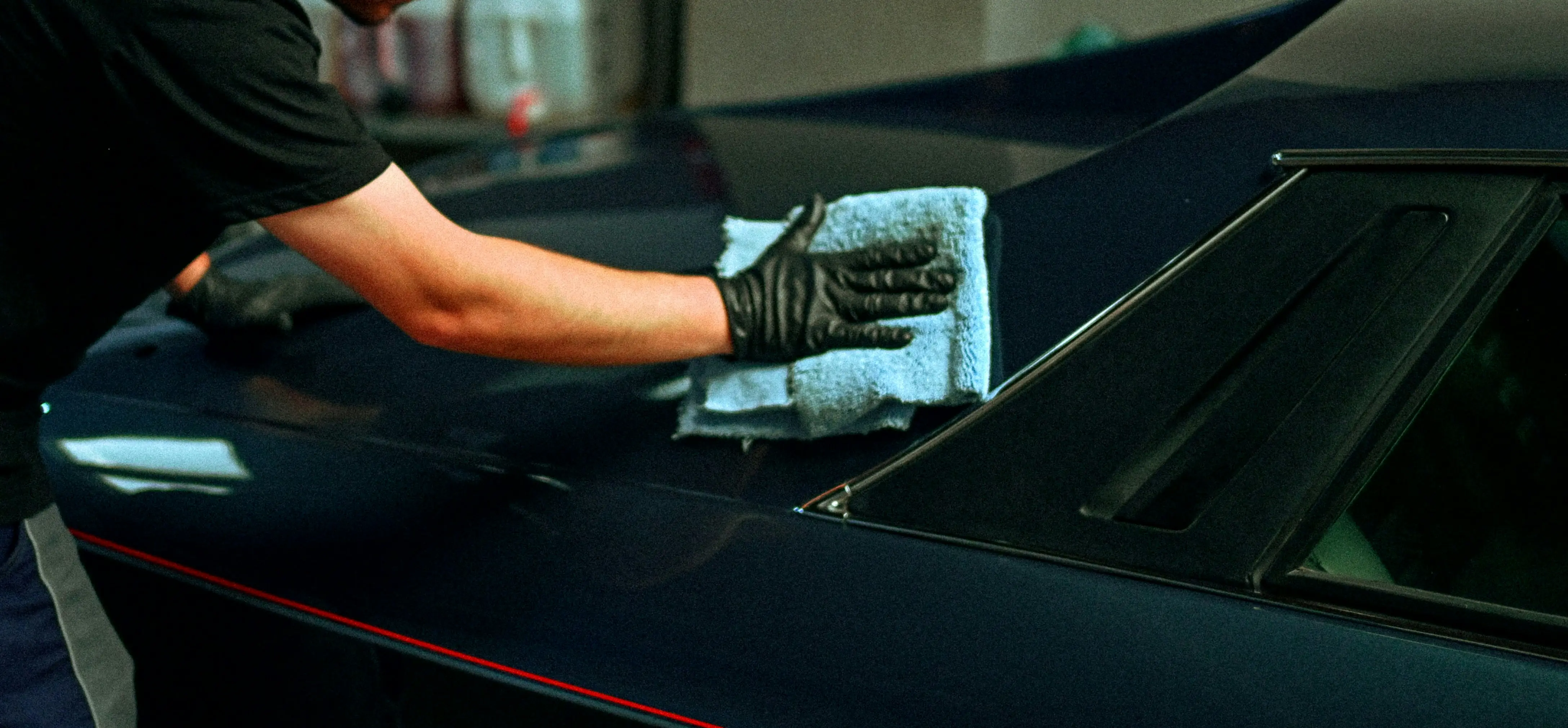 A person polishing a dark blue car with a cloth.