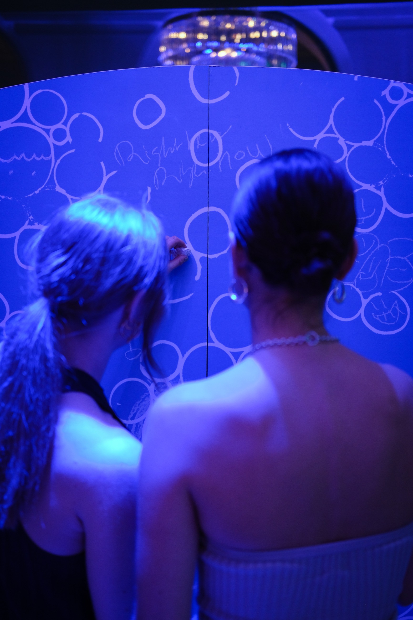 Two guests drawing circles on a blue-lit wall