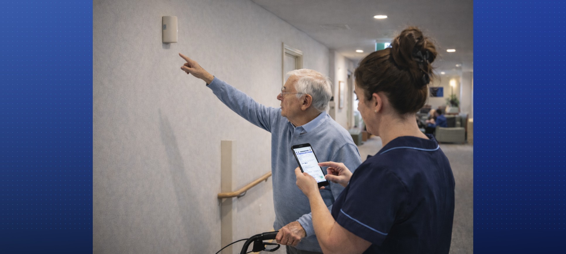 An aged care staff member using mobile maintenance software to log a request while an elderly resident points to a wall fixture, demonstrating efficient and responsive facility management.