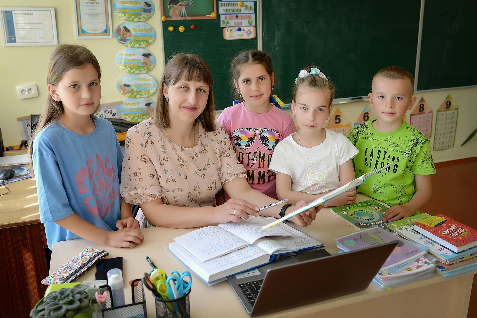 Middle school teacher kneeling beside a student's desk to have a quiet, private conversation during a lesson.