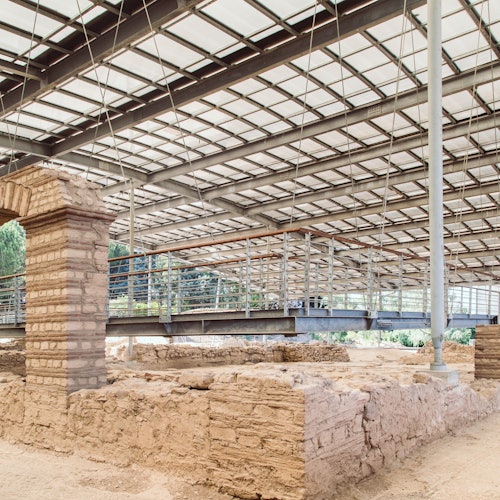 在现代金属和玻璃屋顶下的古代遗址，其中有砖砌结构，背景中有高架人行道。