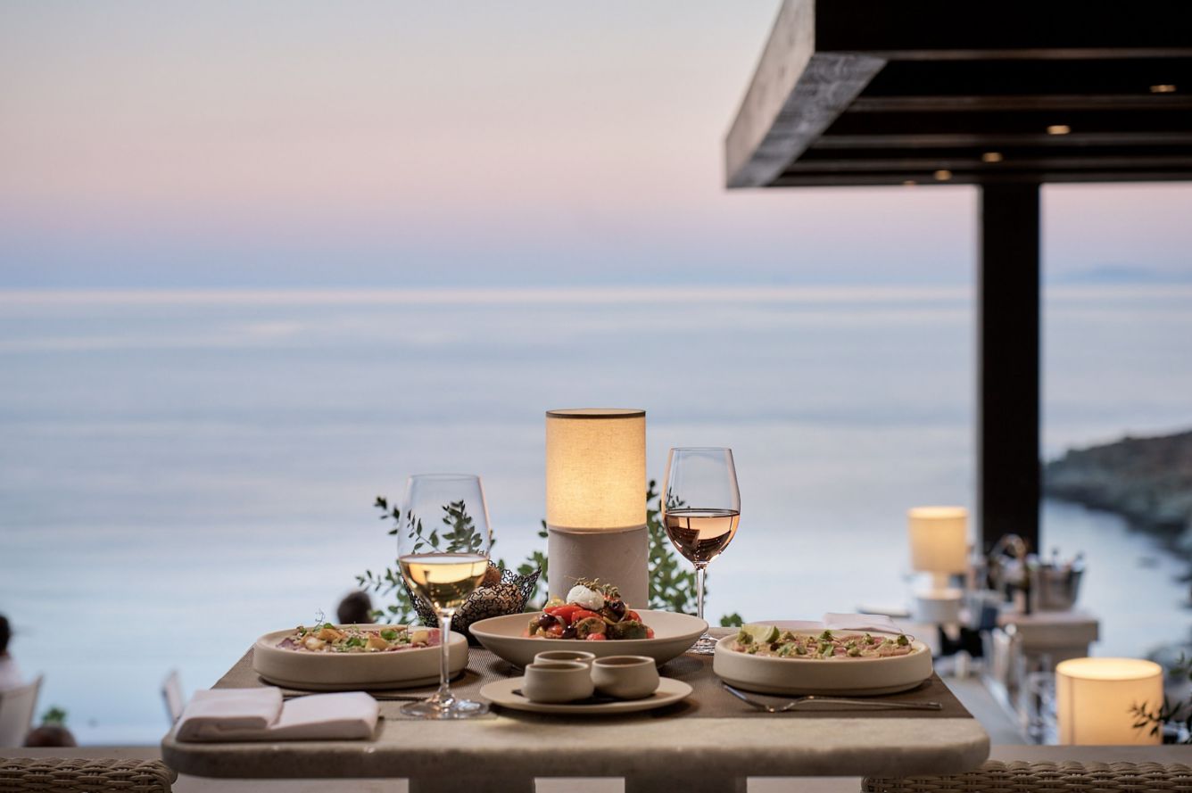 Romantic dinner table set for two with wine and appetizers at dusk against the backdrop of the vast, calm sea.
