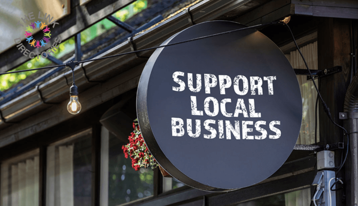 A smiling man with curly hair is sitting at a desk, looking at the camera, with a laptop and a lamp in the background.