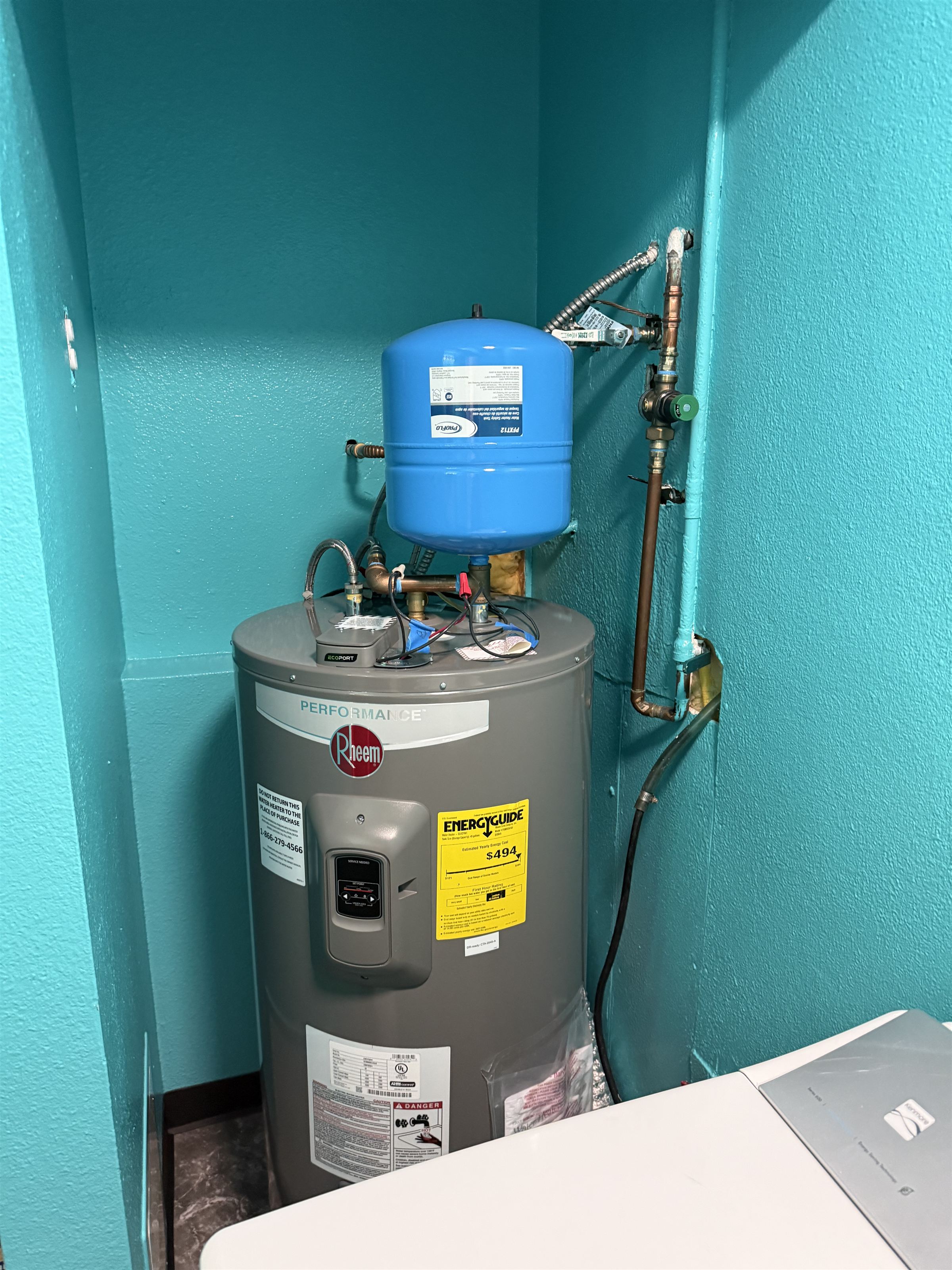 Electric tank water heater with a blue expansion tank and copper piping in a teal alcove