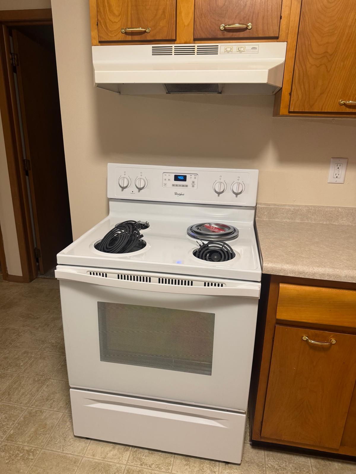 A person leans out of a window on a brick building, holding a colorful flag and smiling.