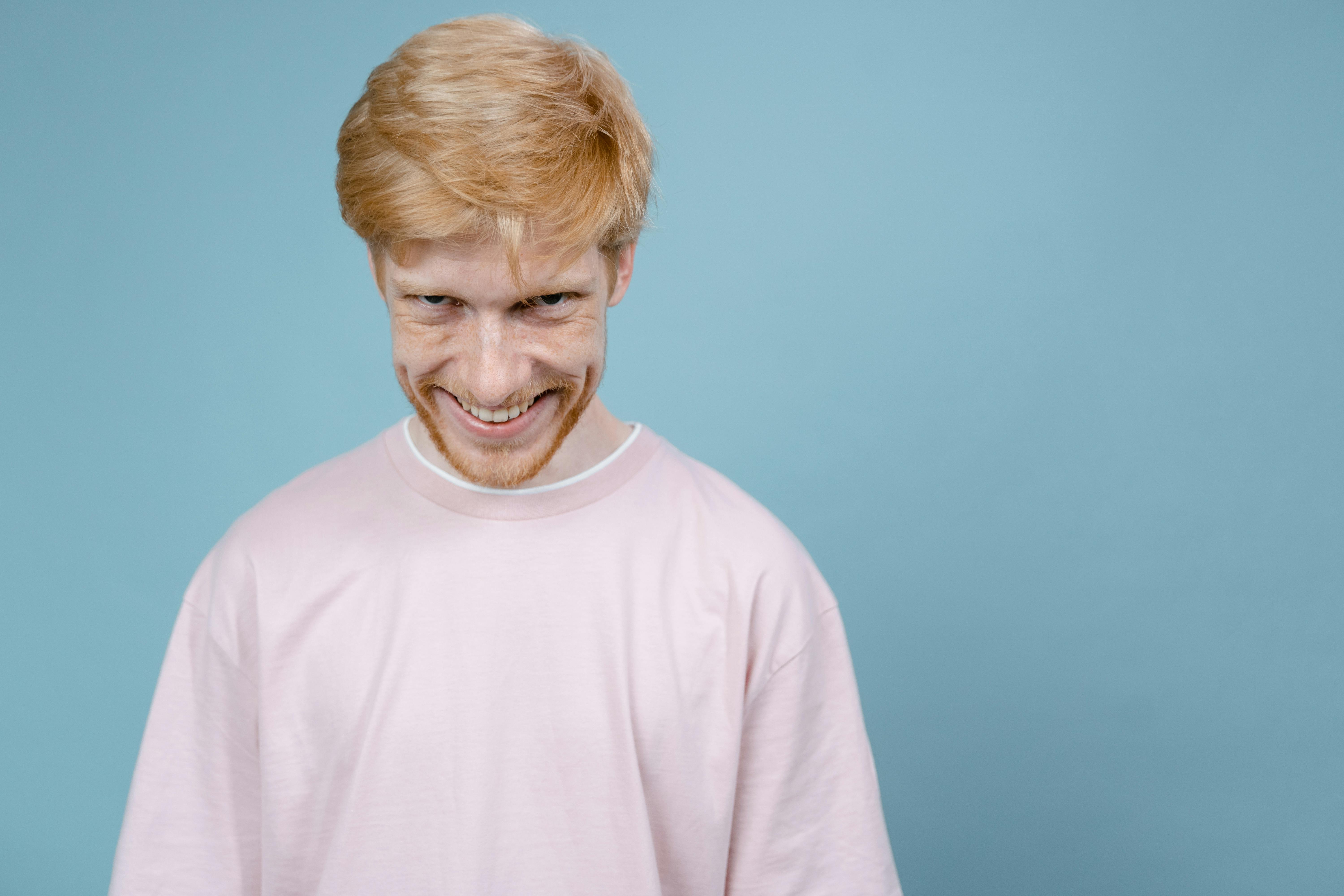 young-man-in-pink-shirt-smiles-mischievously-against-blue-background-in-studio-s - tima-miroshnichenko (pexels)